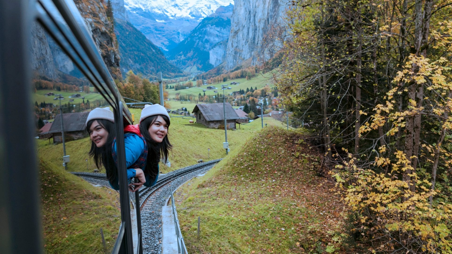 a girl sticks her head outside the window as the train passes through the Swiss Alps
