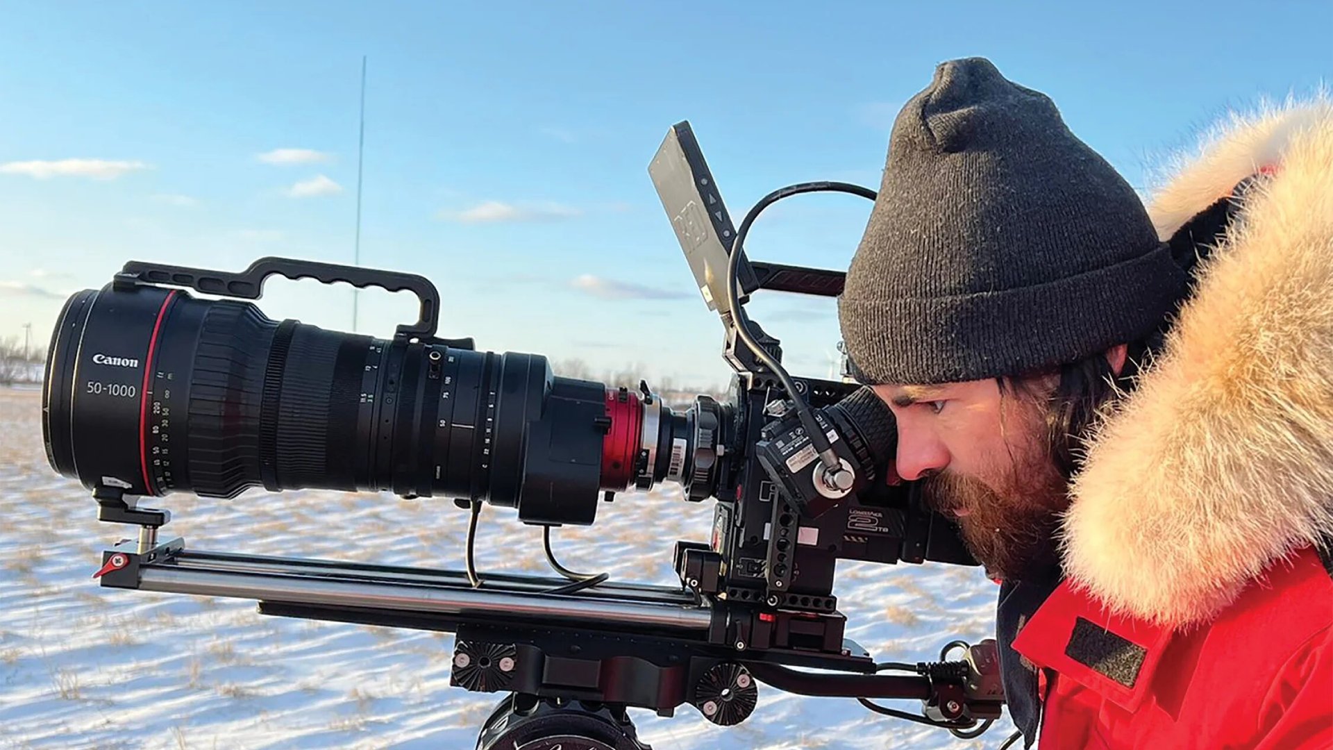 a man in a red parka operates a digital cinema camera in a snowy landscape