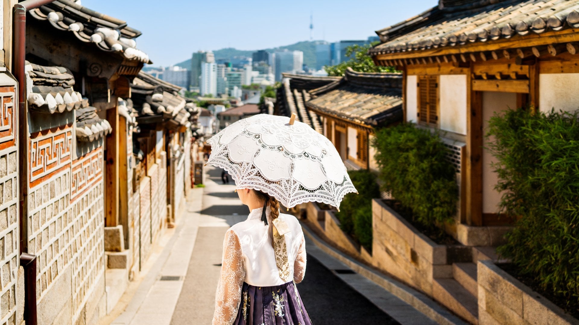 a woman with a parasol and traditional dress walking through Bukchon Hanok Village in Seoul, South Korea