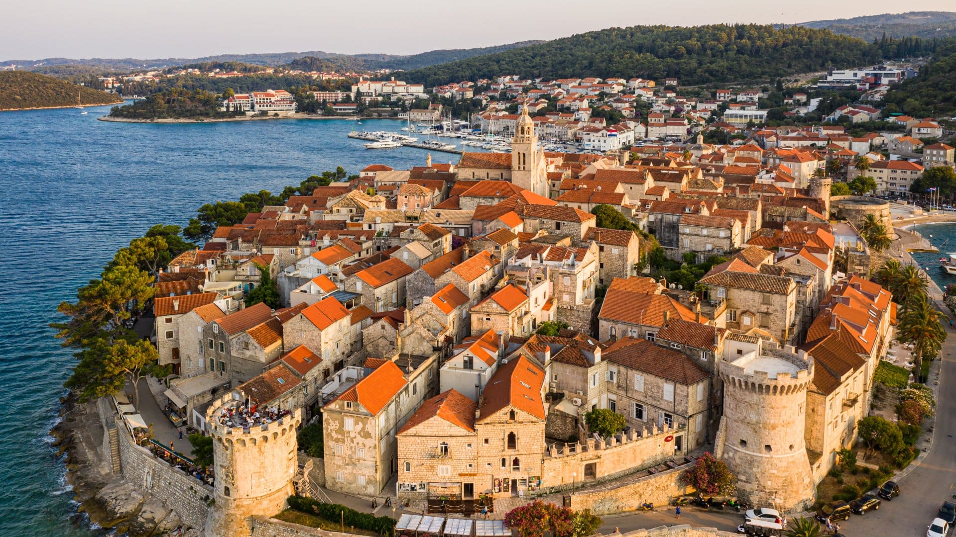 an aerial view of red-roofed homes and medieval walls surrounding the Croatian city of Korcula