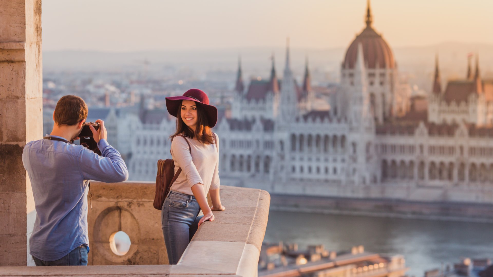 man taking photo of woman overlooking river with city backdrop