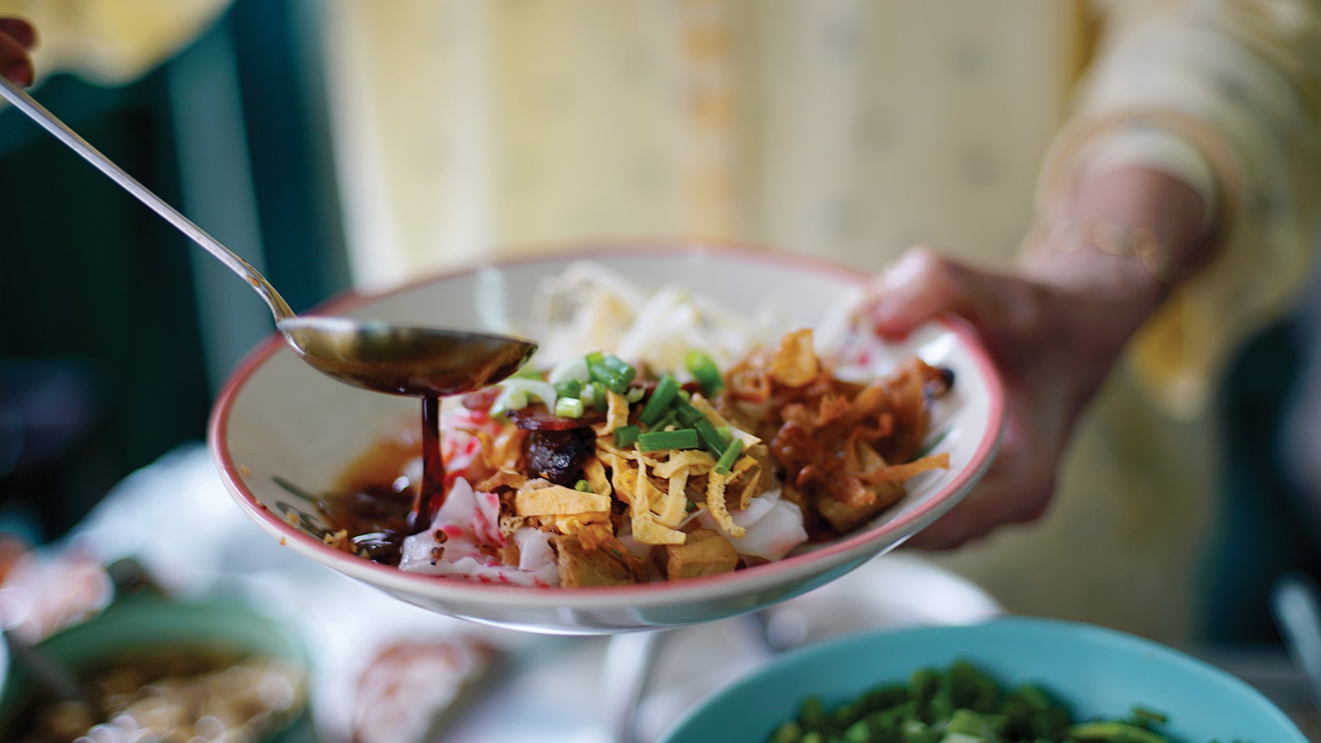 Merchant cook soy sauce on top of delicious Chinese steamed rice noodle rolls, beautifully arranged in white plate ready to serve customer in local restaurant in Thailand