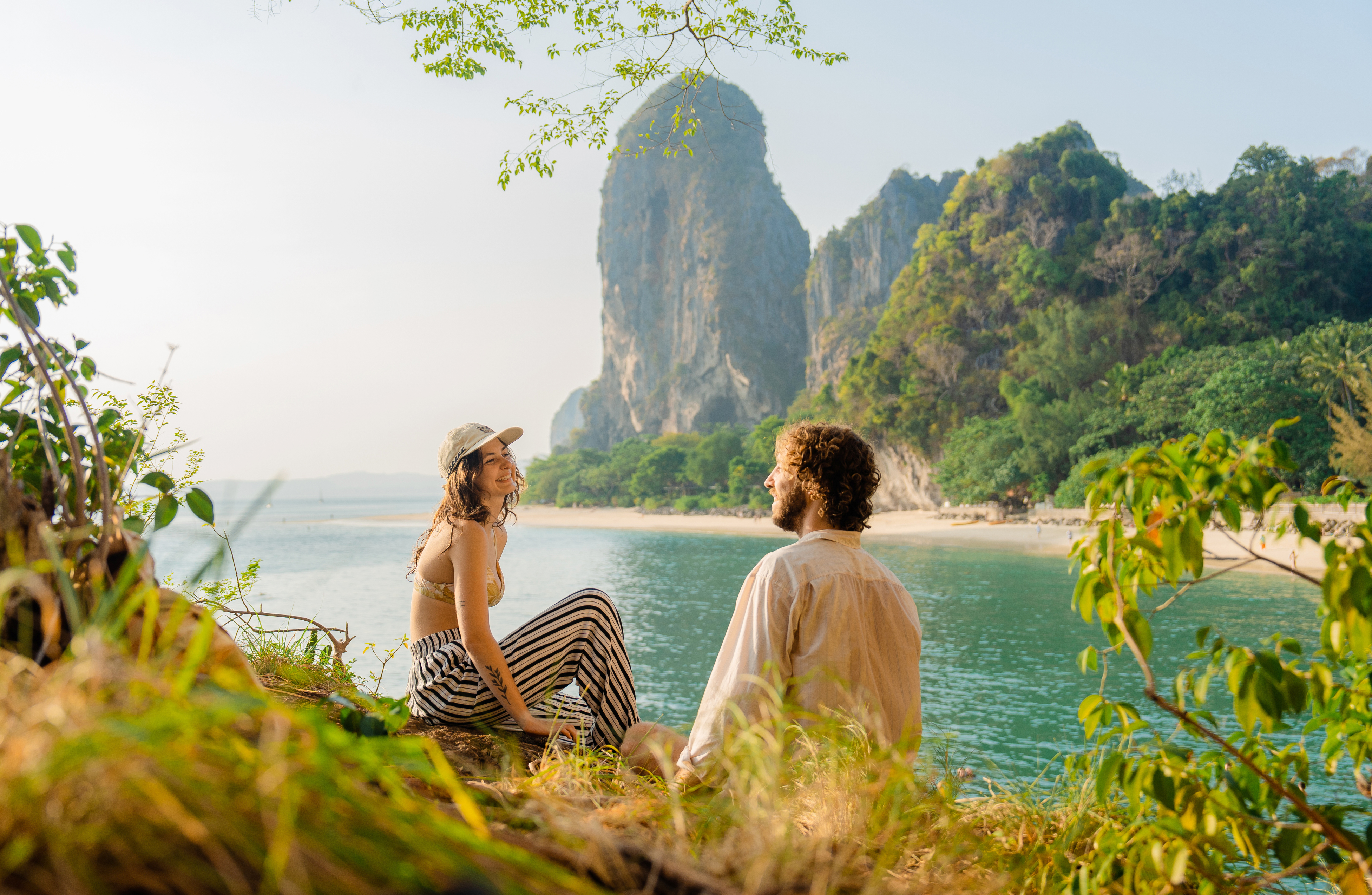 A smiling couple in the foreground overlooking Raleigh Beach, Thailand.