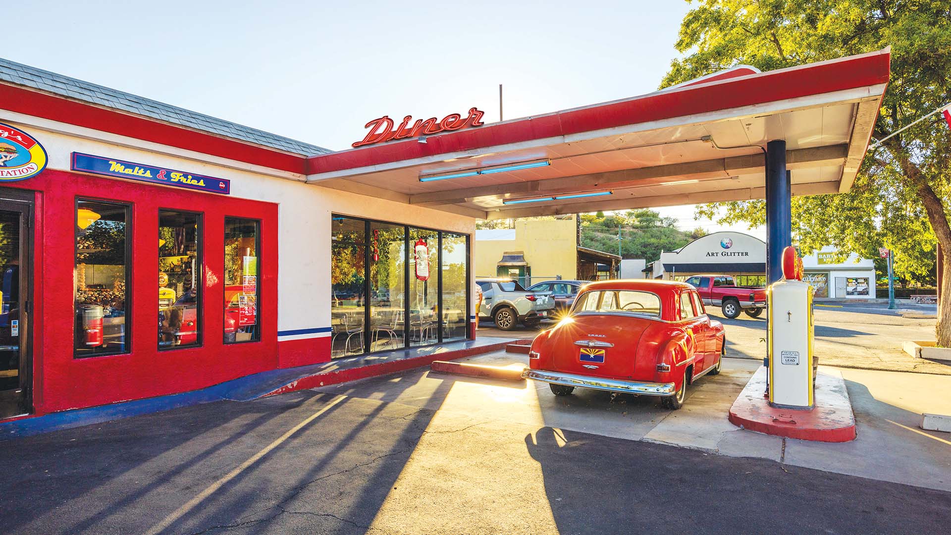A vintage car at a gas station next to an old diner in middle America