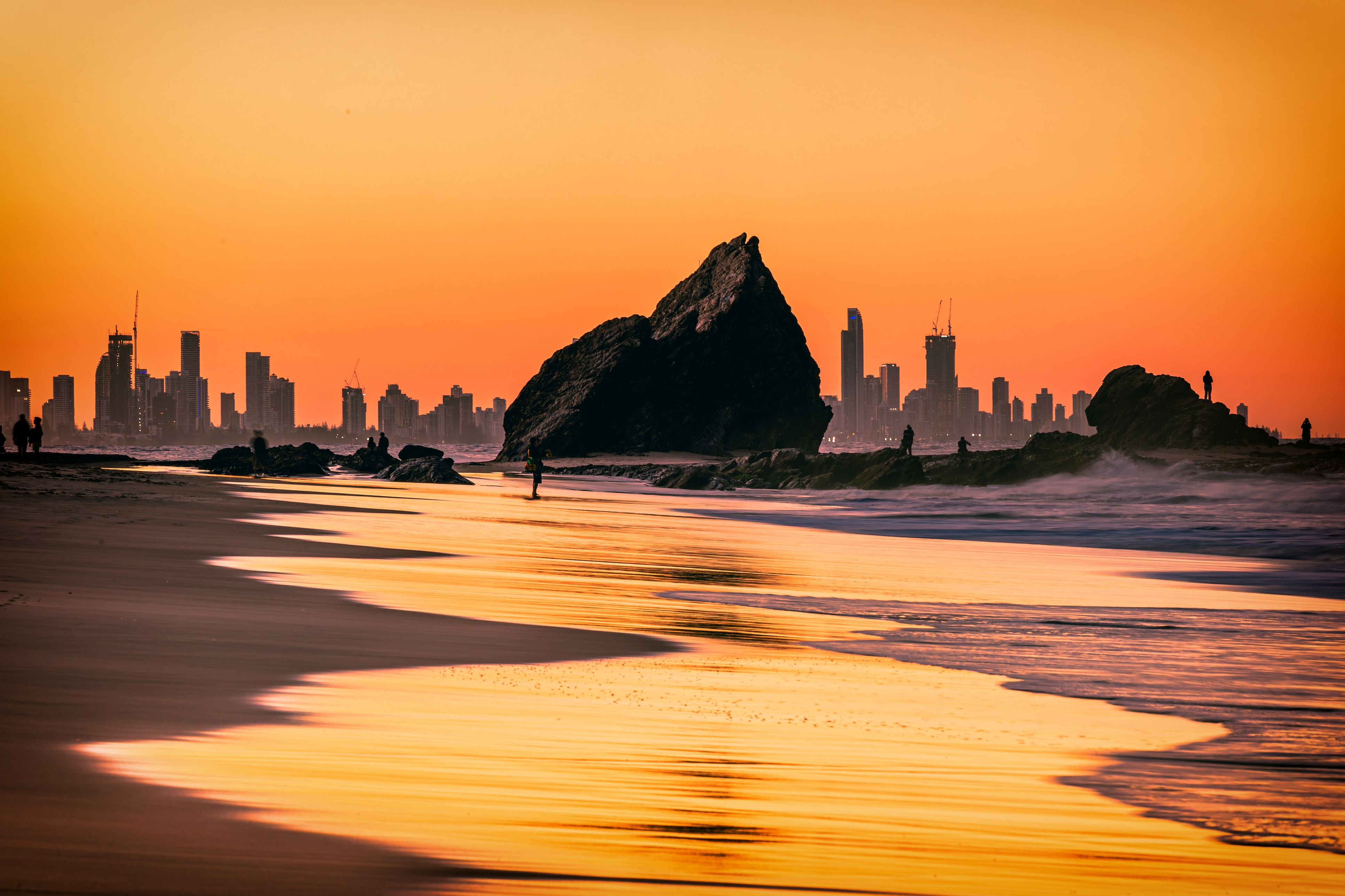 The sunset view of the Currumbin Beach in the twilight and the urban skyline of Gold Coast in the distance
