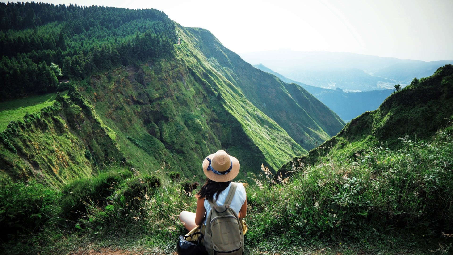 woman sitting on edge of hillside overlooking green mountains