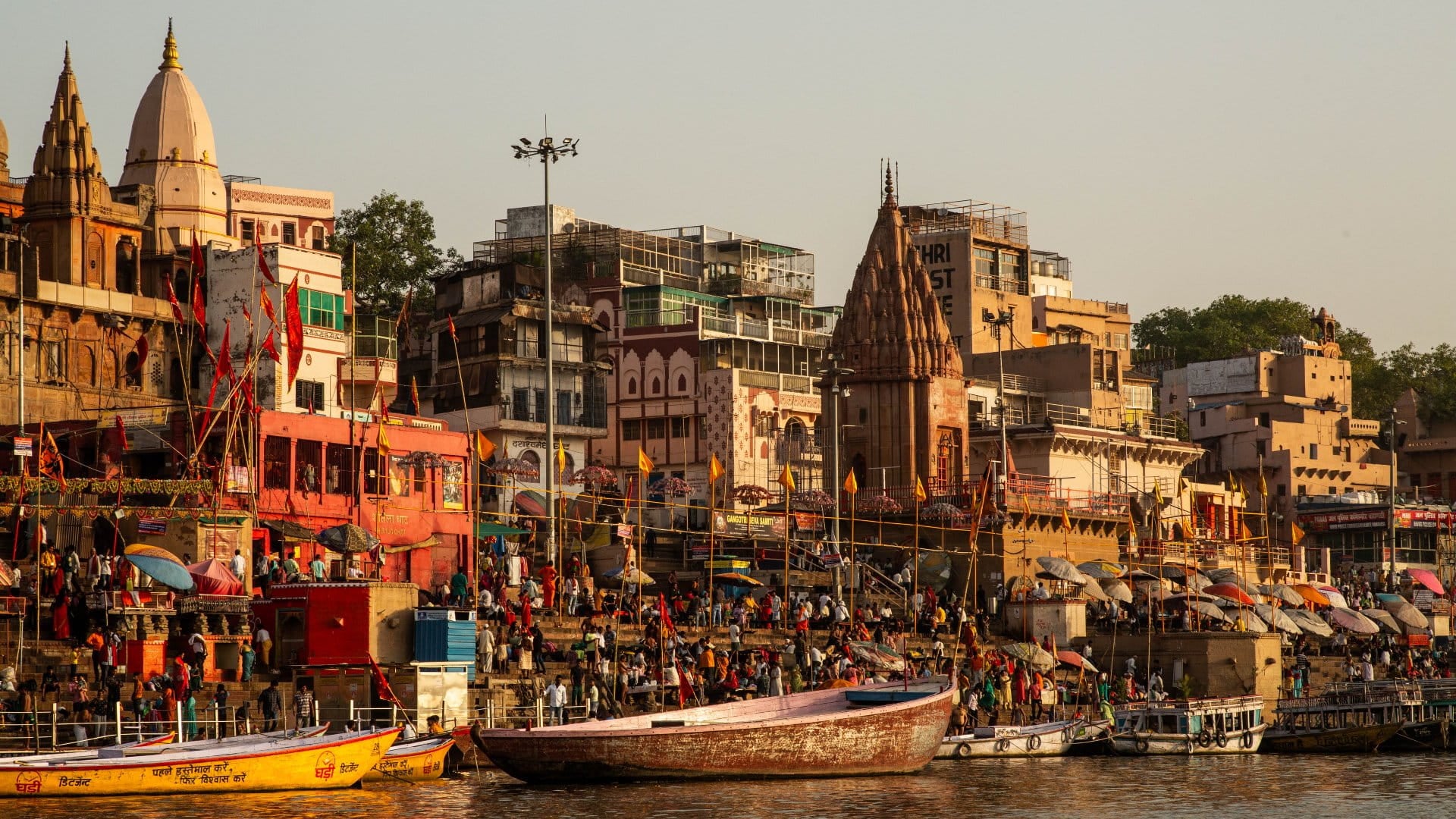 View of the Ganges River with the ghats leading down and boats on the river, as well as pilgrims crowding its edges in Varanasi, India.