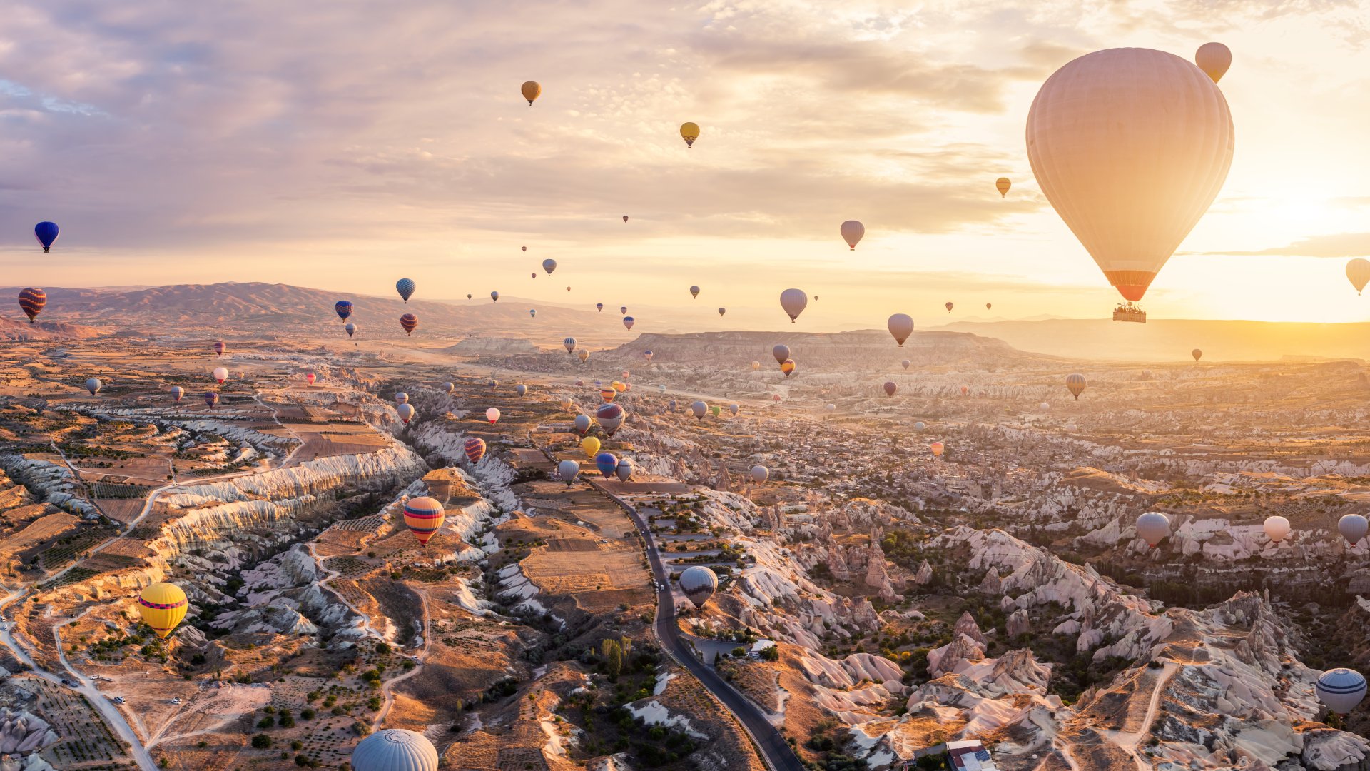 Hot air balloons rise over the fairy tale chimneys of Turkiye's Cappadocia against sunrise