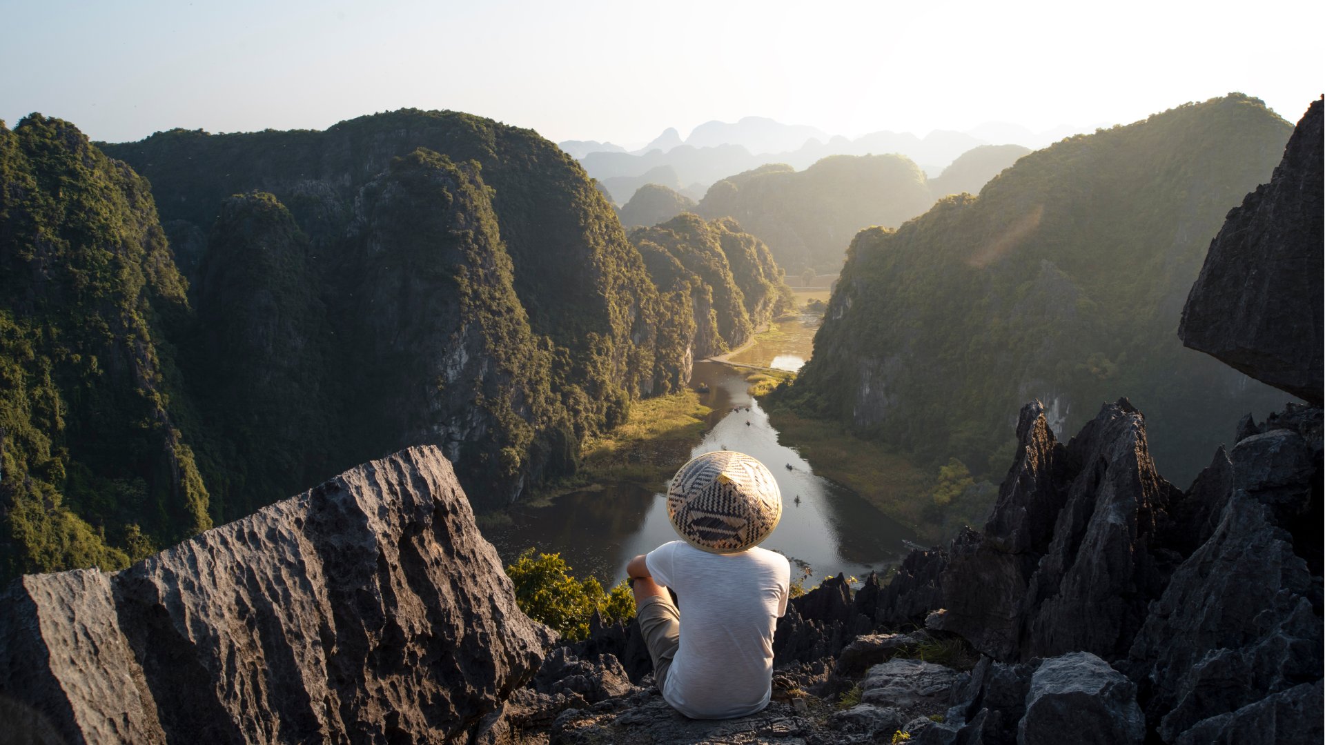 Ninh Binh, Vietnam man in a straw hat sitting on the edge of a mountain overlooking river