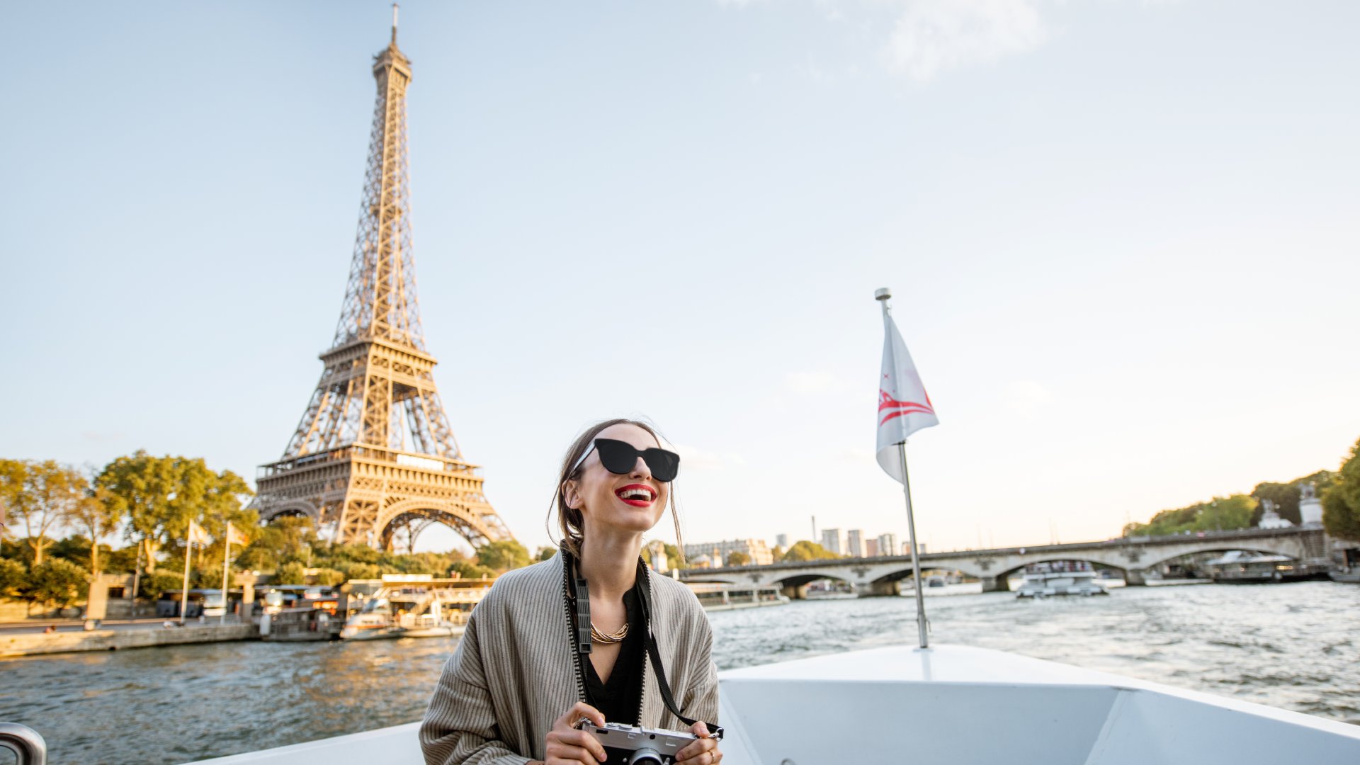 woman with camera on a river boat alongside landmarks