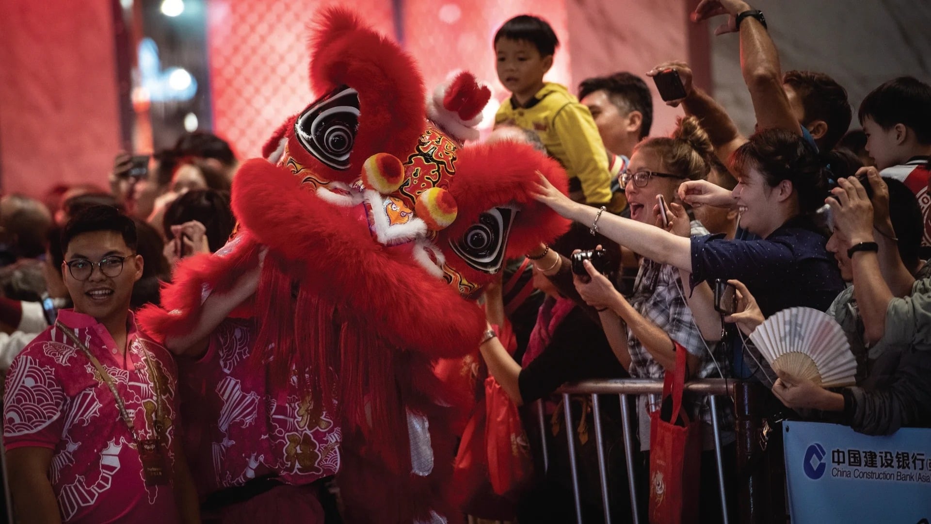 Crowds celebrate at a festival with a vivid red lion dance costume and festive atmosphere.