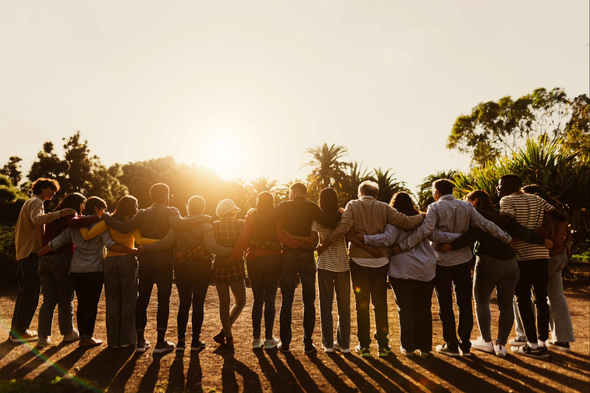 A large group of travellers embrace while watching a sunset