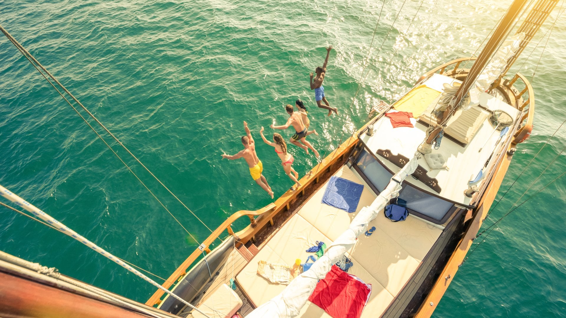 Aerial view of group of people jumping from sailing boat on a day sea trip