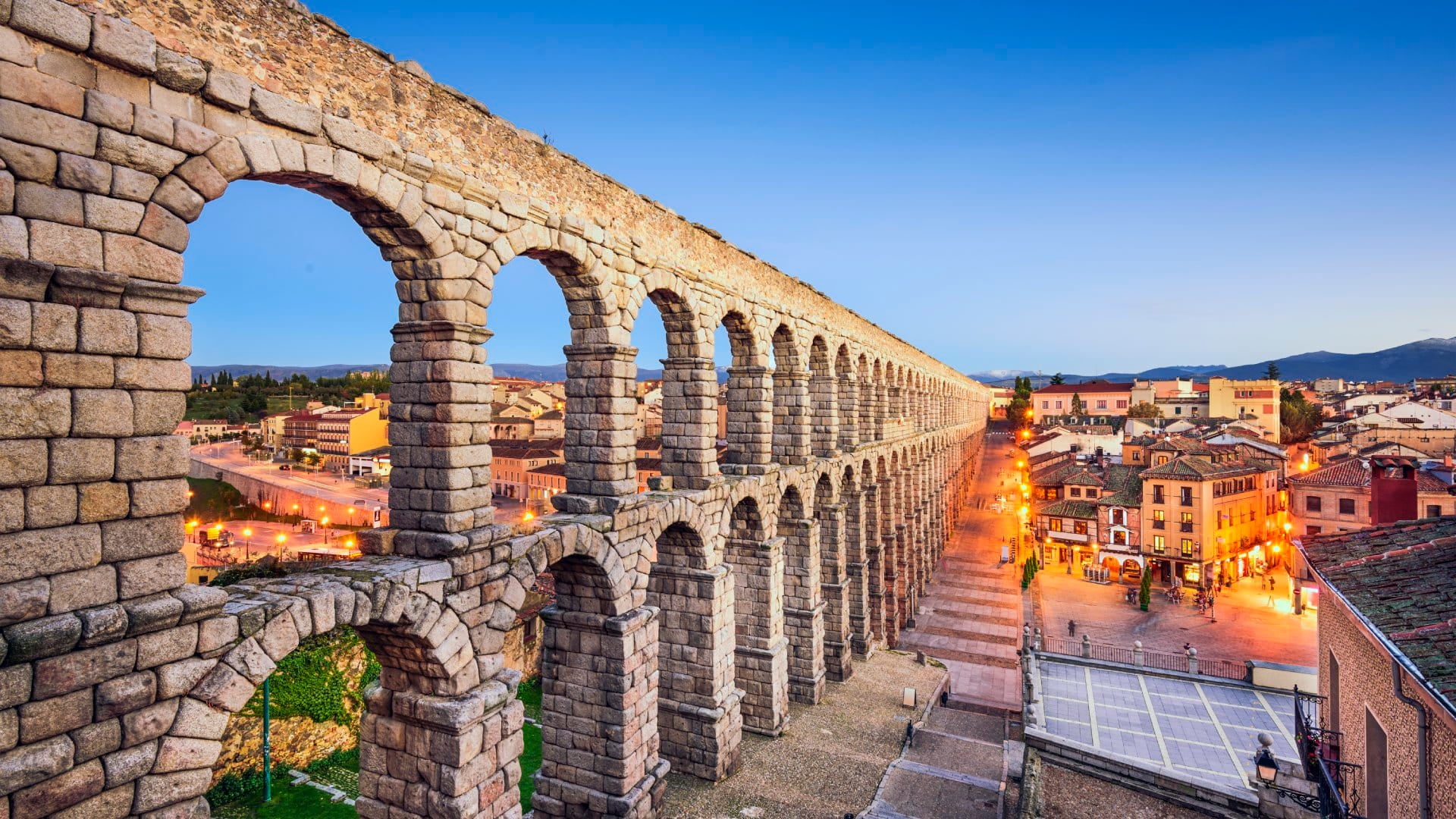 Ancient Roman aqueduct cutting through ancient village at twilight.