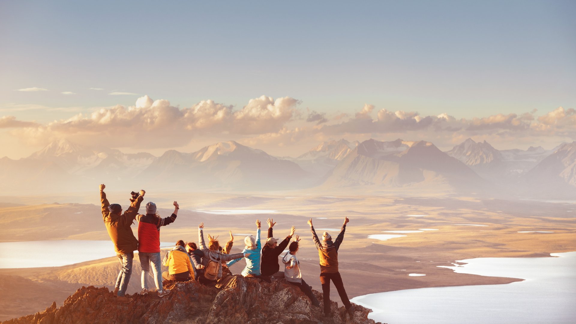 Group celebrating hiking to reach top of mountain top looking out at mountain's valley