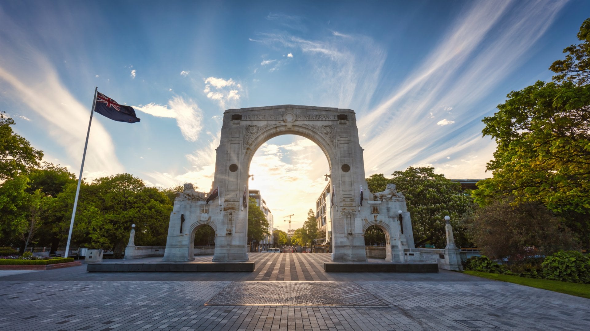 Sunset Panorama of the famous Bridge of Remembrance in Christchurch with New Zealand Flag blowing in the wind. Arch backlit against the sunset Sun