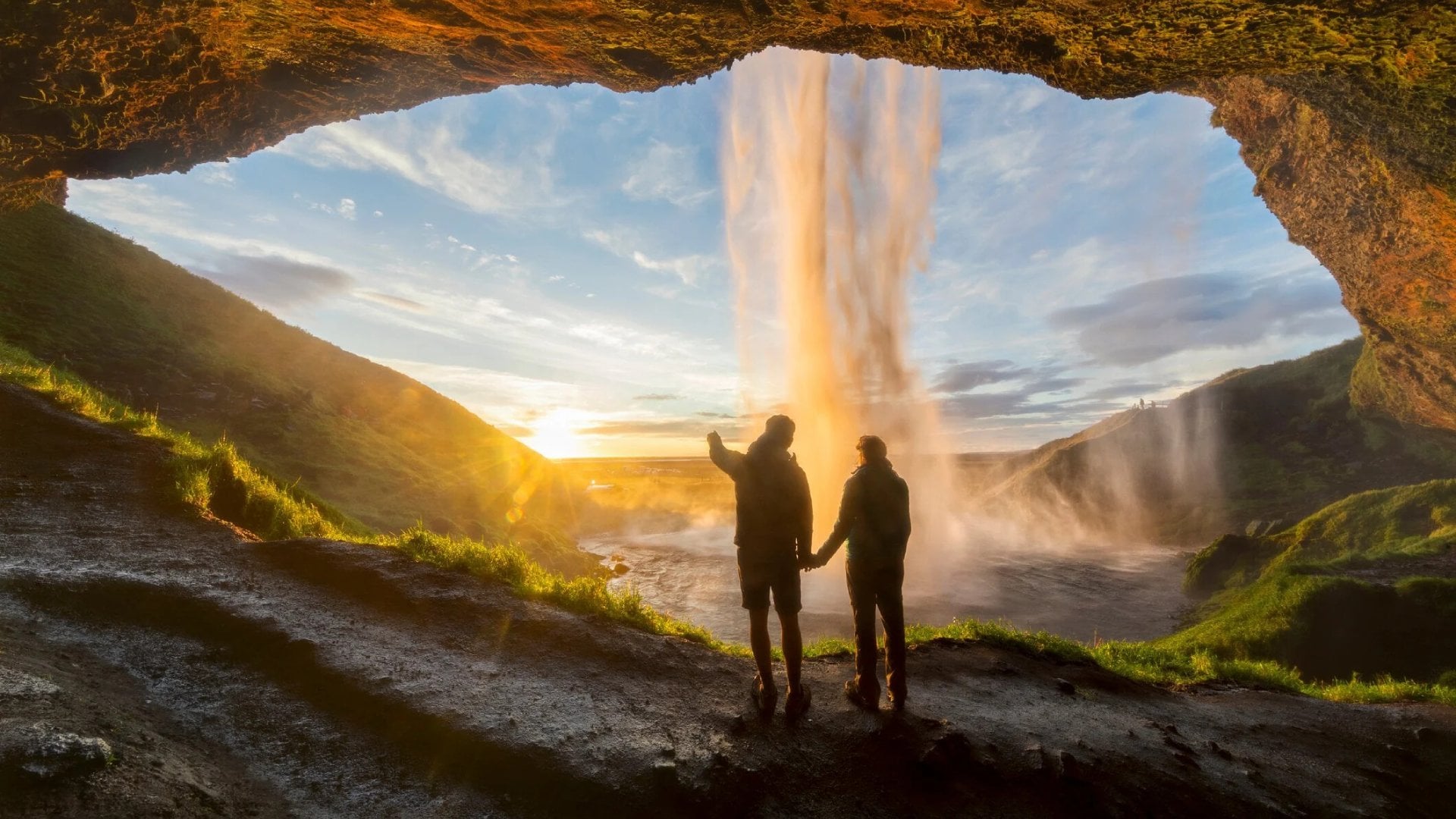 Tourists under waterfall in Seljalandsfoss, Iceland, man pointing with finger to the sun