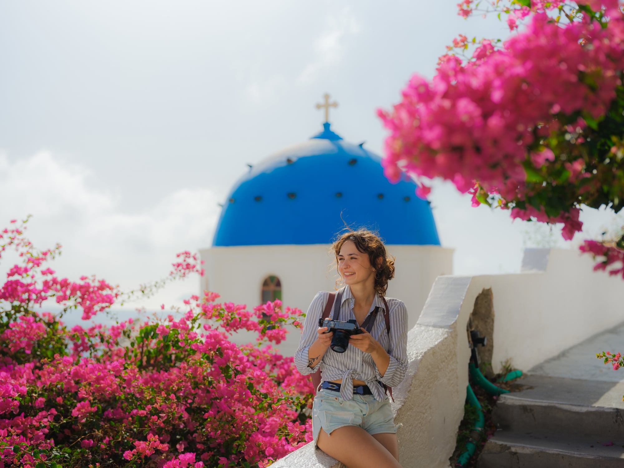 A woman leaning on the edge of a walkway in Oia on Santorini in Greece with bouganvillea blooming