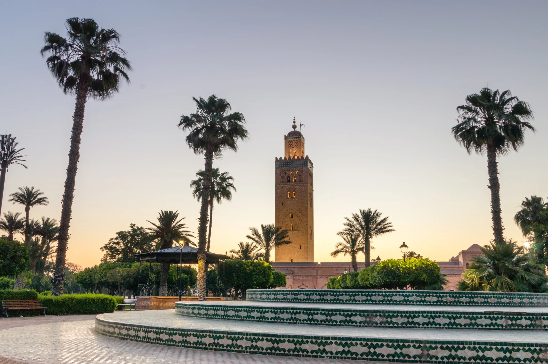 A view of a tall tower surrounded by palm trees and greenery at sunset.