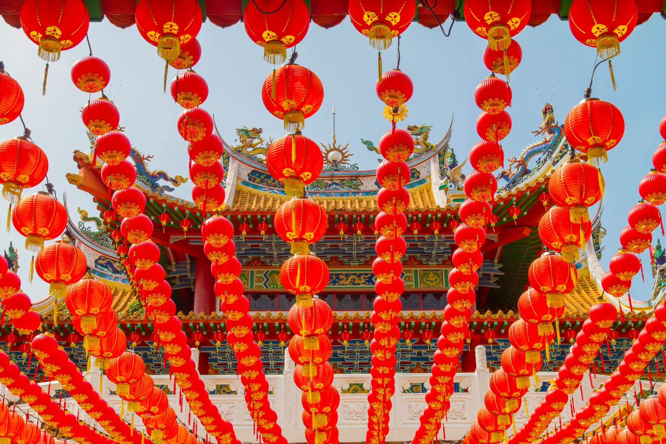 A vibrant display of red lanterns hanging in front of a decorative building, celebrating a festive occasion.