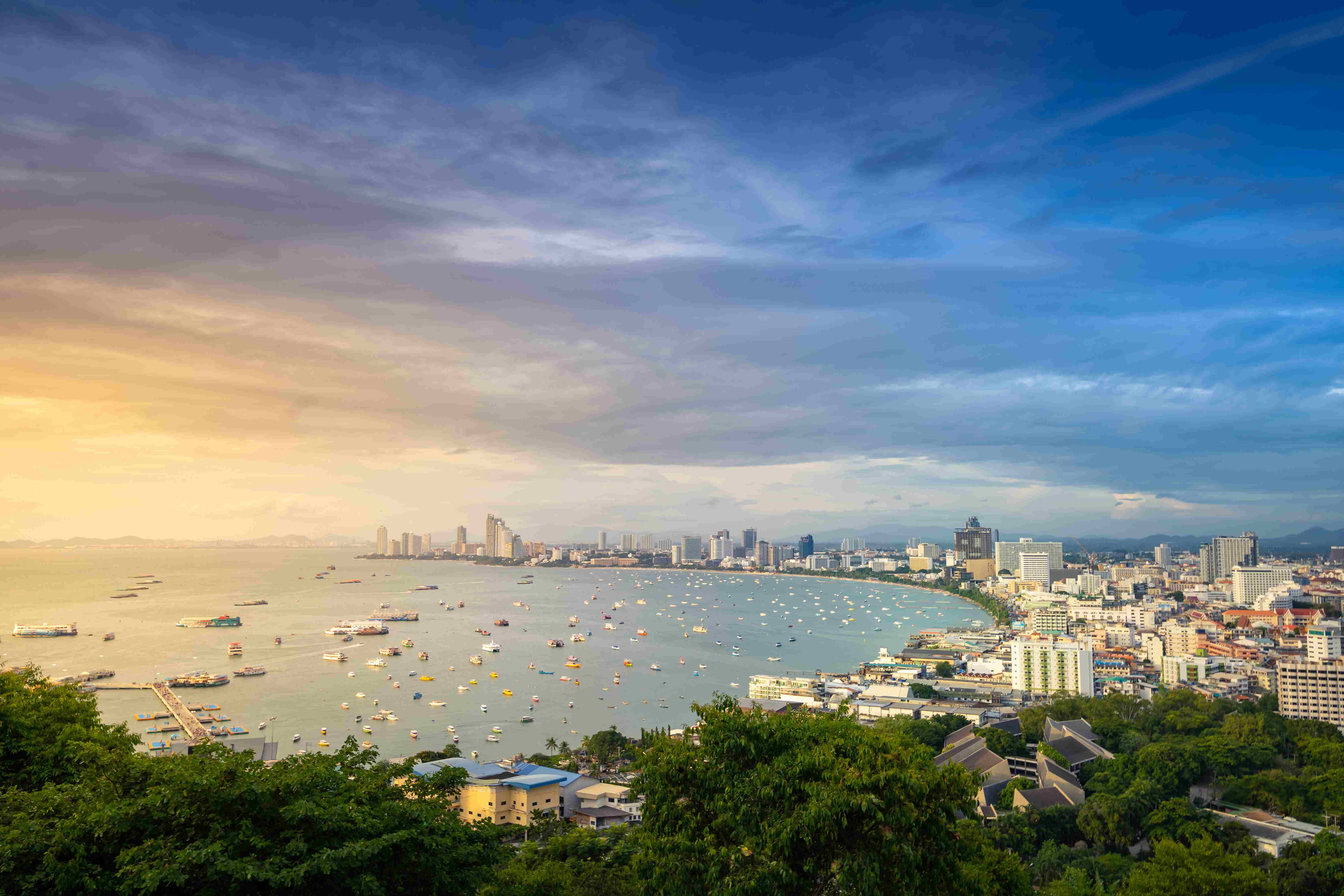 Bang Lamung District Arieal sunset view of boats in water and buildings along curved coastline of Pattaya city