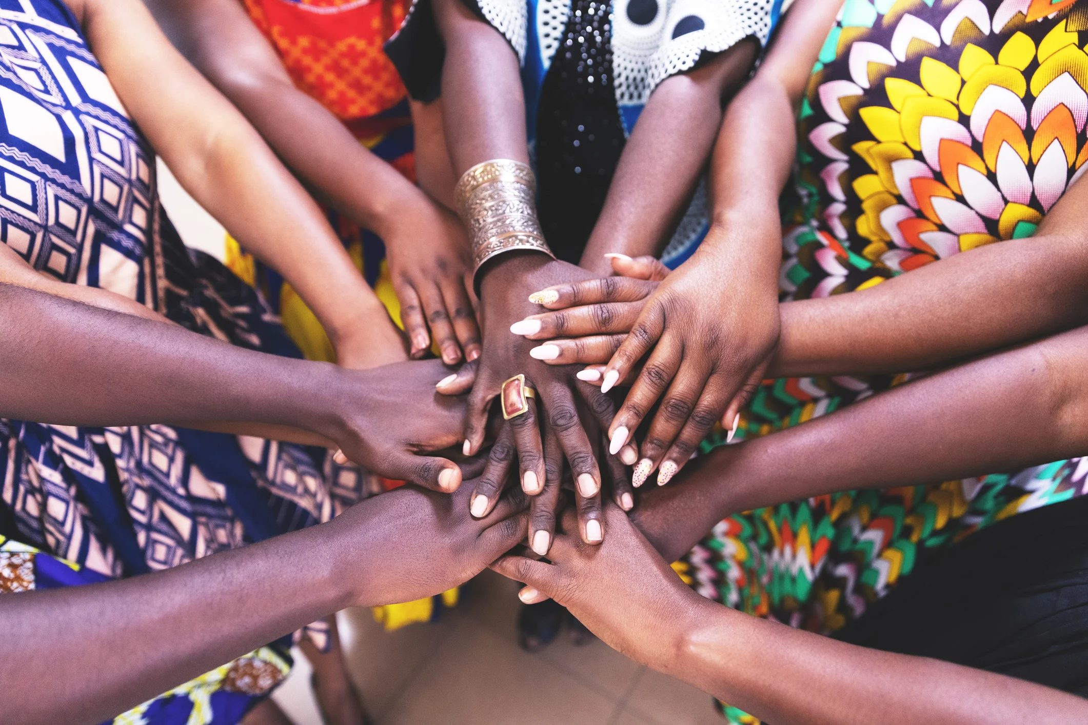 A circle of diverse hands overlapping each other, showcasing unity and collaboration with colorful patterns in the background.
