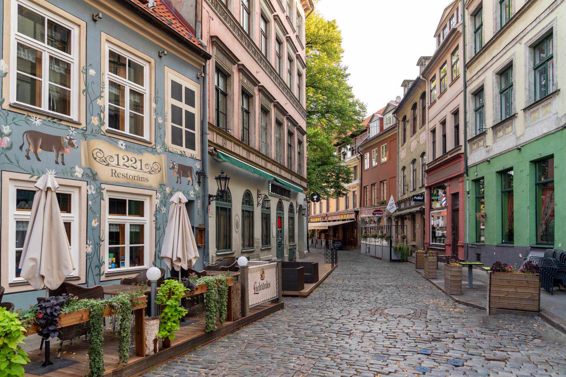 Charming cobblestone street lined with colorful buildings and outdoor restaurant seating under clear skies.