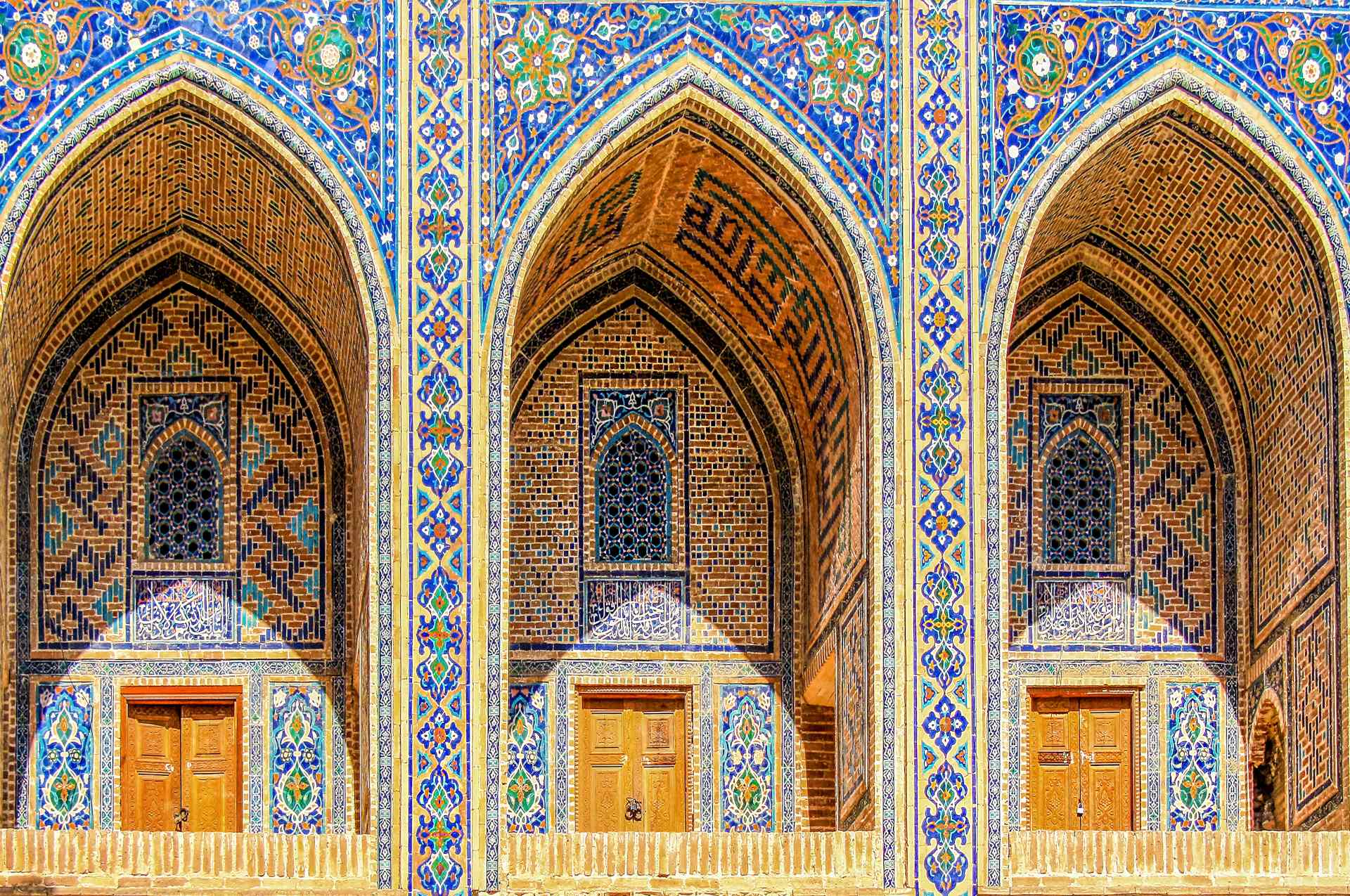 Sherdor Madrassah facade with blue, yellow and green tiles, wall with tall arches and windows