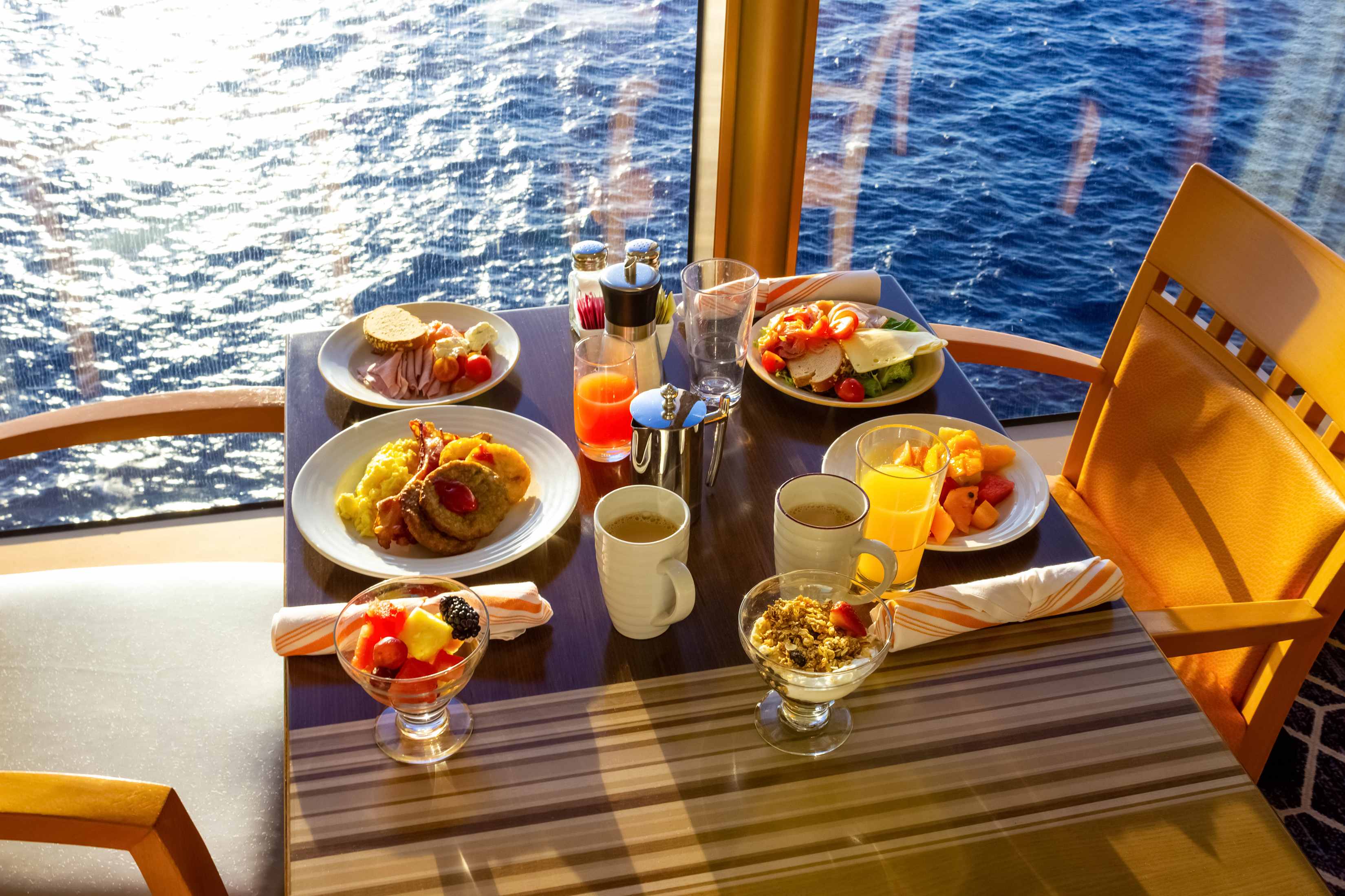 A table set with various breakfast dishes and drinks, overlooking the ocean through large windows.