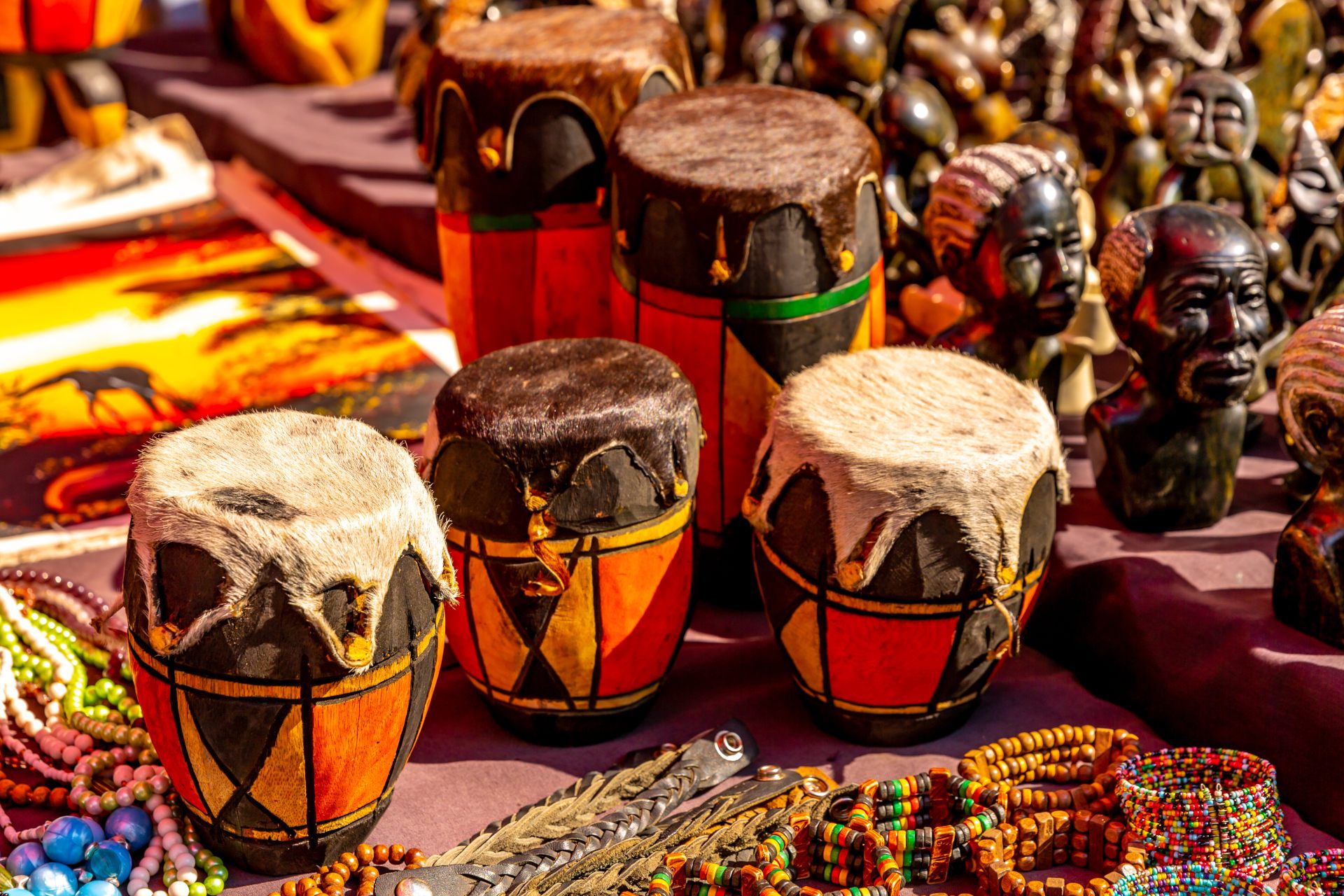 Colorful handmade drums with fur tops surrounded by beads and carved figures at a market.