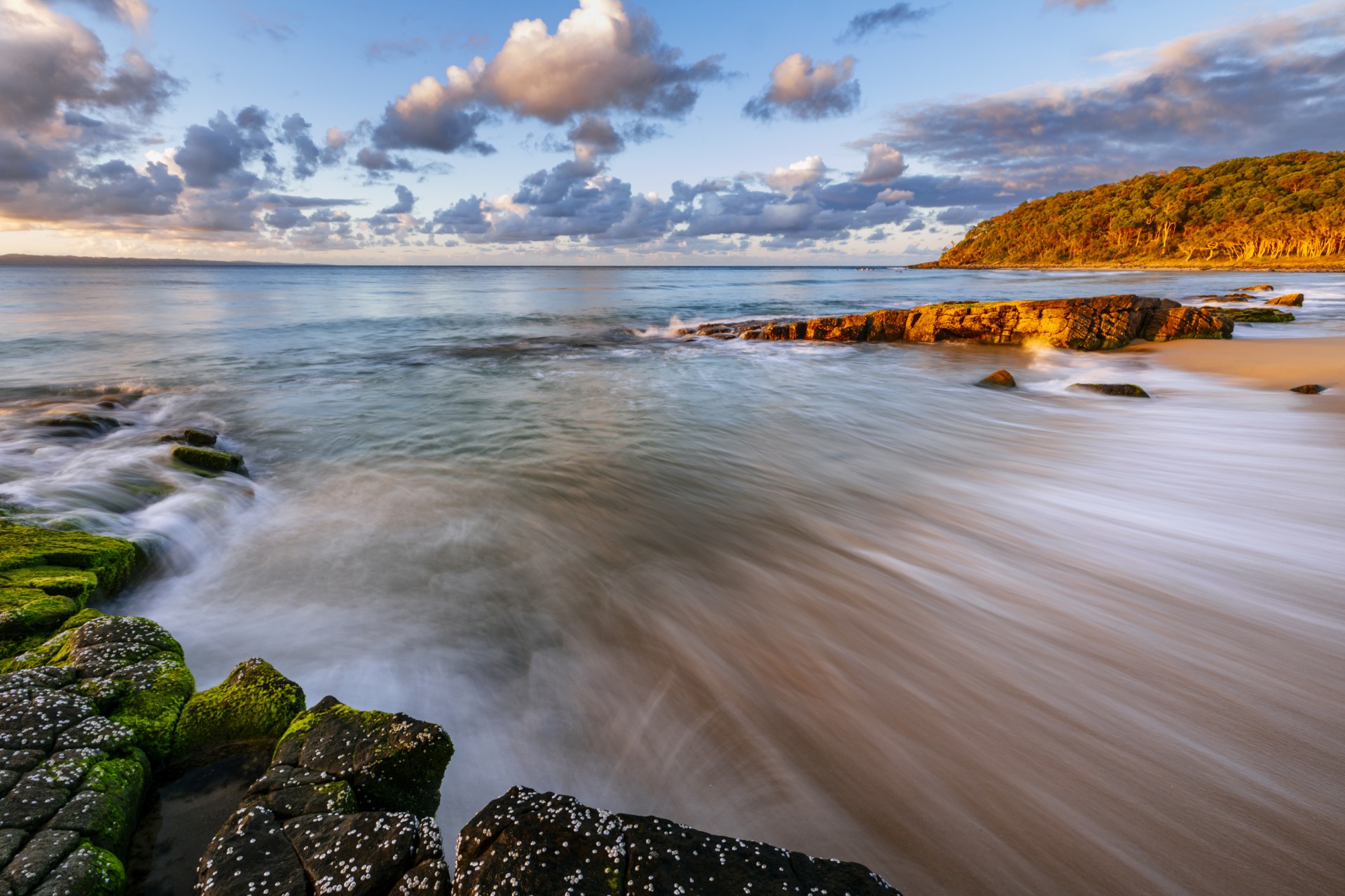 Water crests the shoreline at sunset