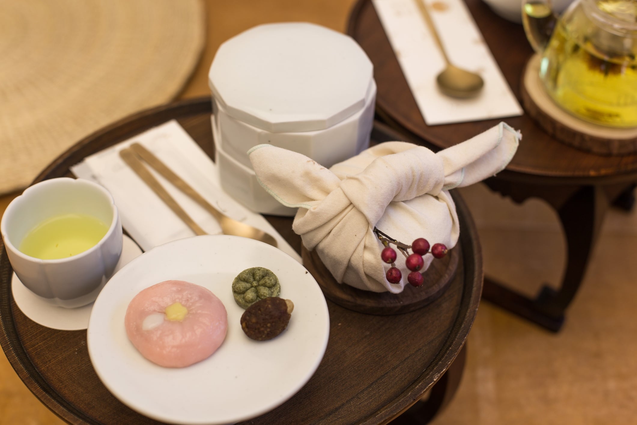 Tea and sweets displayed on a wooden table: green tea, traditional snacks, and a wrapped treat in cloth.