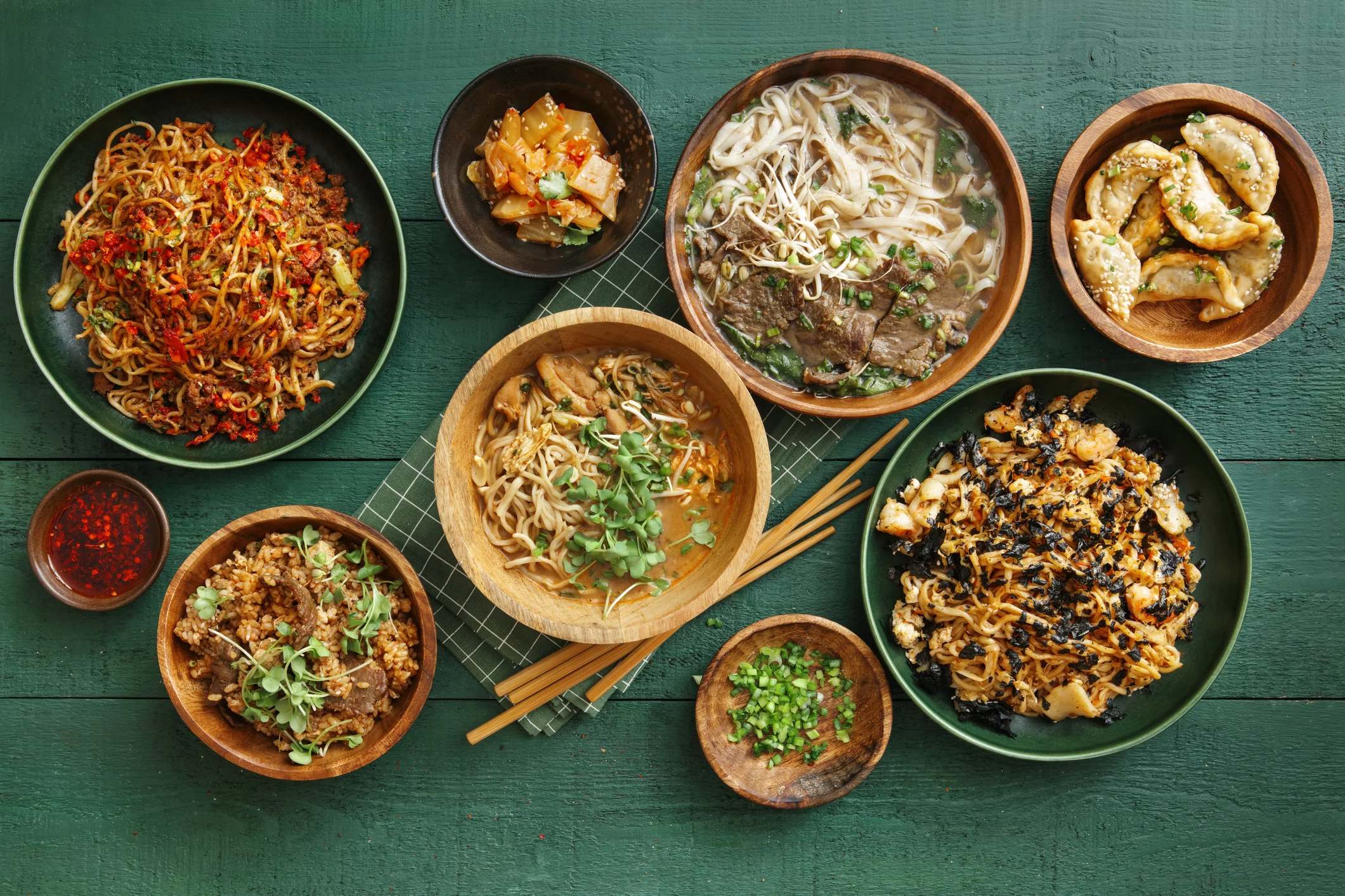 A spread of various Asian dishes including noodles, dumplings, and stir-fried vegetables on a green table.