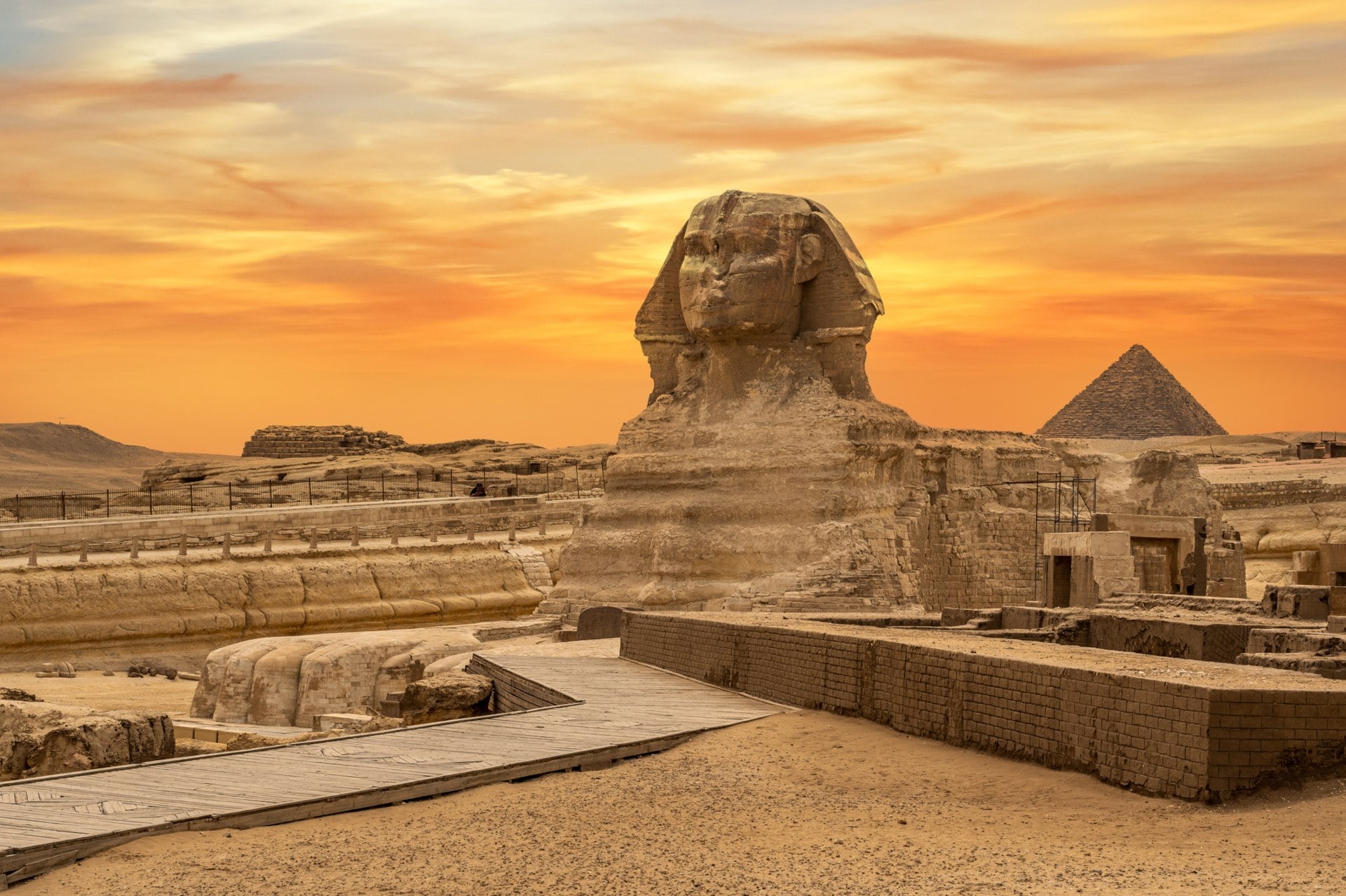 The Great Sphinx of Giza at sunset, with the Great Pyramid in the background and desert landscape surrounding.