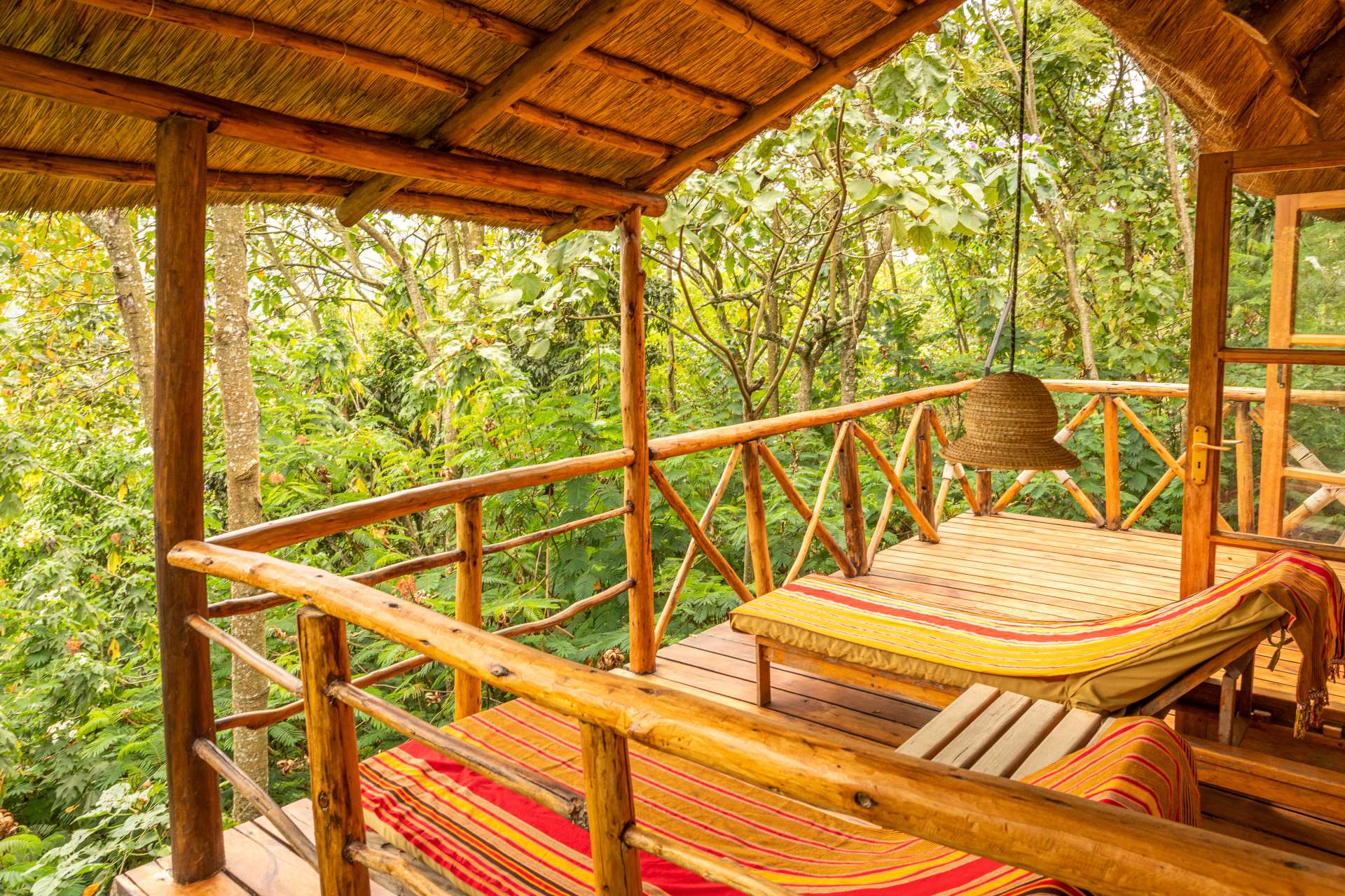 Cozy wooden balcony with striped loungers, surrounded by lush greenery and a hanging light fixture.