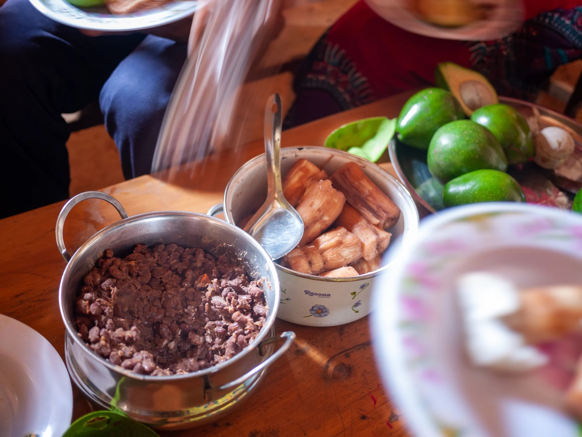 A table with bowls of ground meat and fried plantains, surrounded by fresh avocados and plates of food.