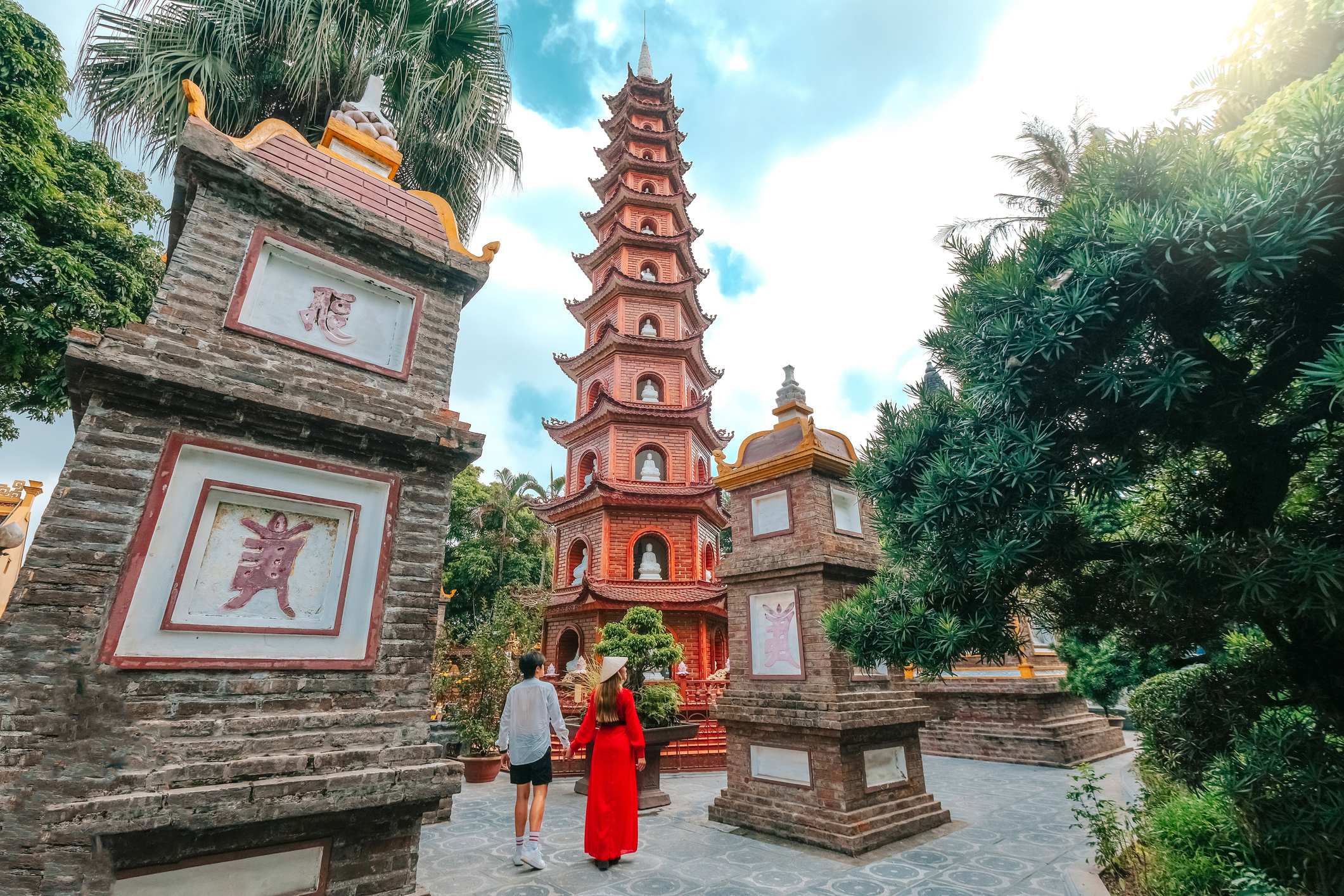 Couple walking towards a tall pagoda surrounded by greenery and traditional stone structures.