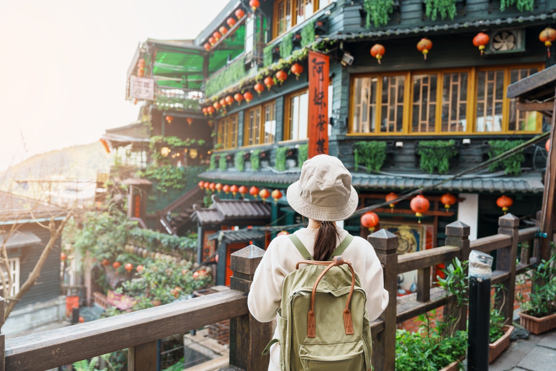 Person in a hat and backpack gazes at a colorful, traditional building adorned with lanterns and greenery.