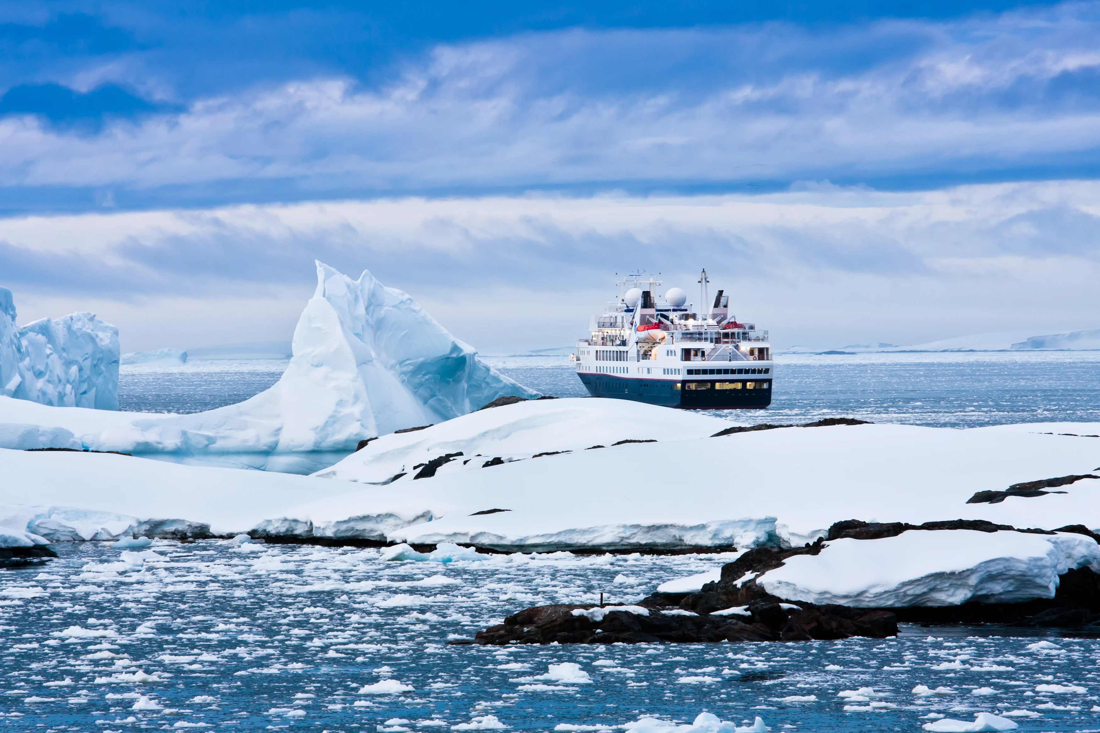 A cruise ship navigates icy waters near large glaciers and floating ice in a serene Arctic landscape.