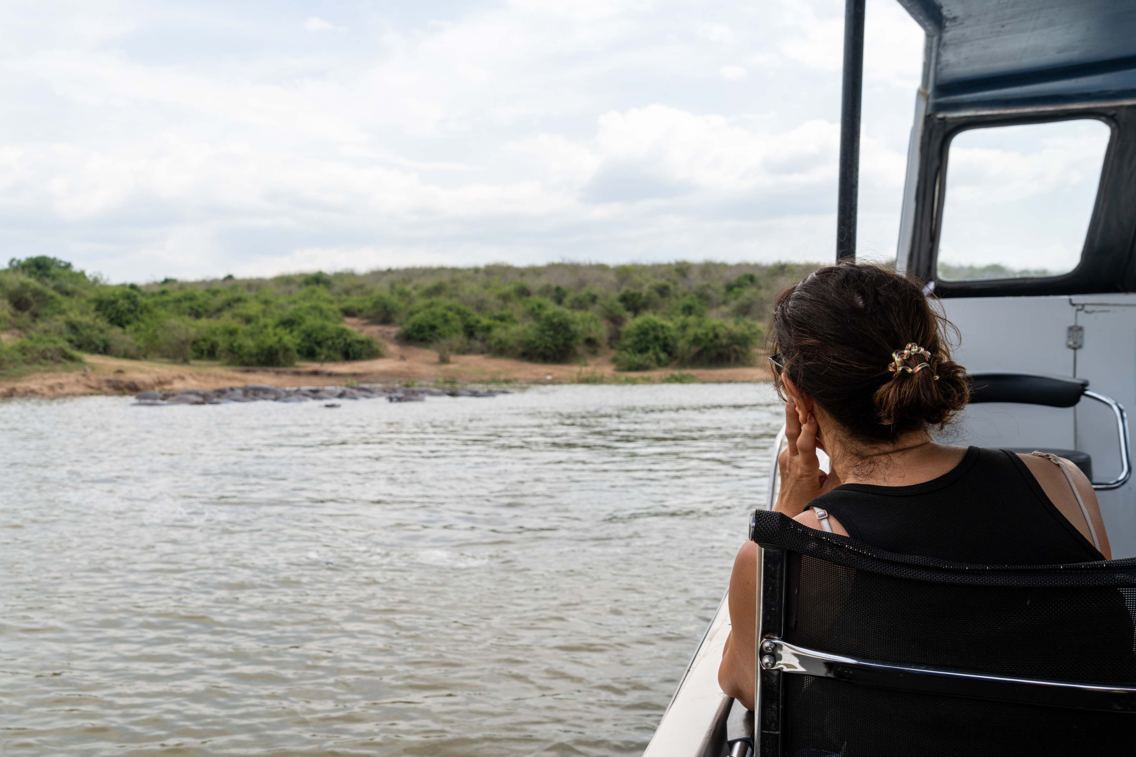 A person sitting on a boat, gazing thoughtfully at the water and surrounding greenery under a cloudy sky.
