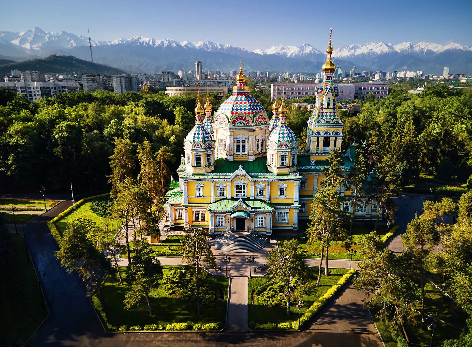 Aerial view of the Zenkov Cathedral in Panfilov Park against blue sky and and snowy mountains in Almaty city, Kazakhstan
