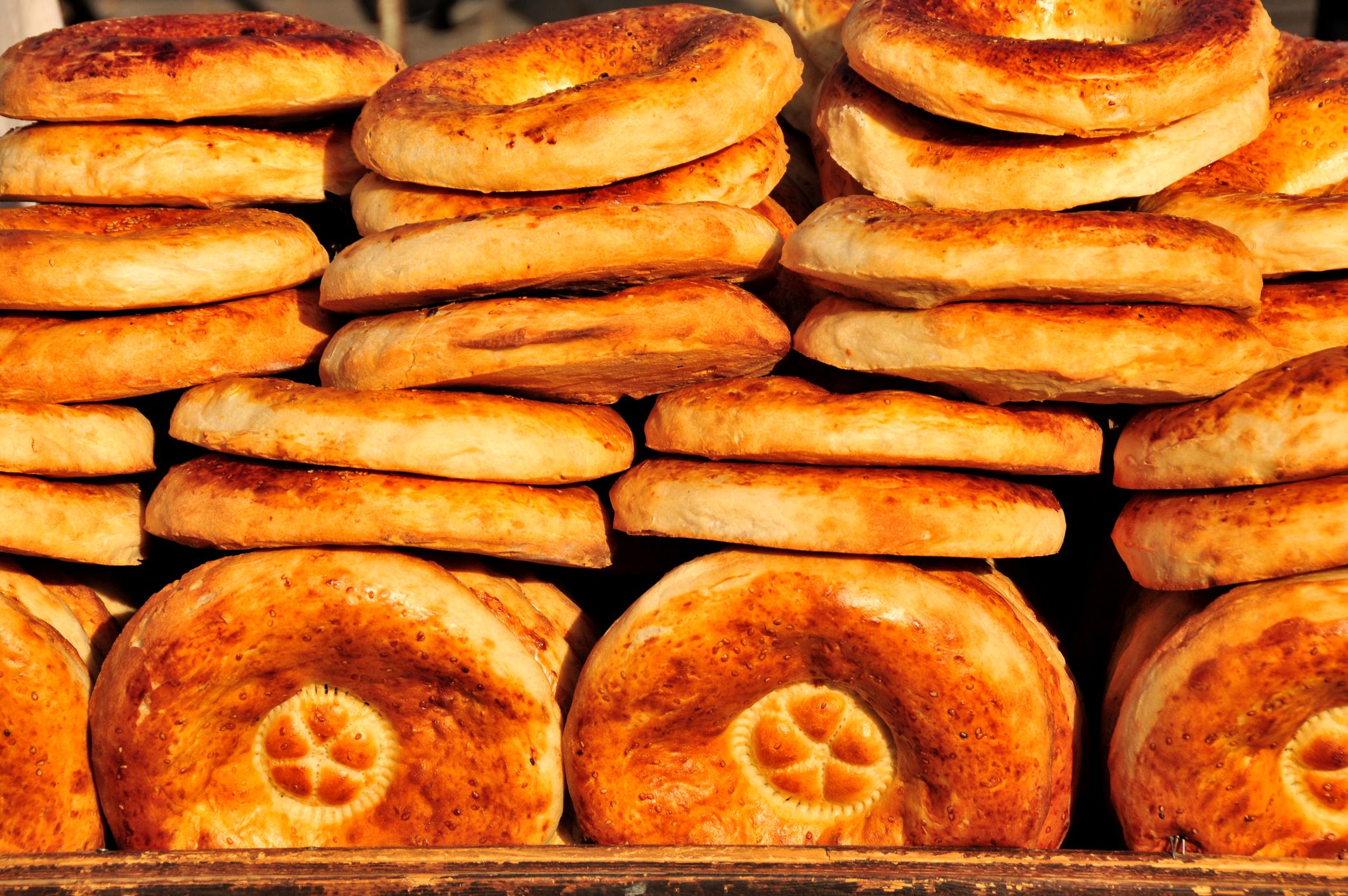 A stack of freshly baked round bread, golden brown with a slightly crisp surface and a decorative pattern on top.