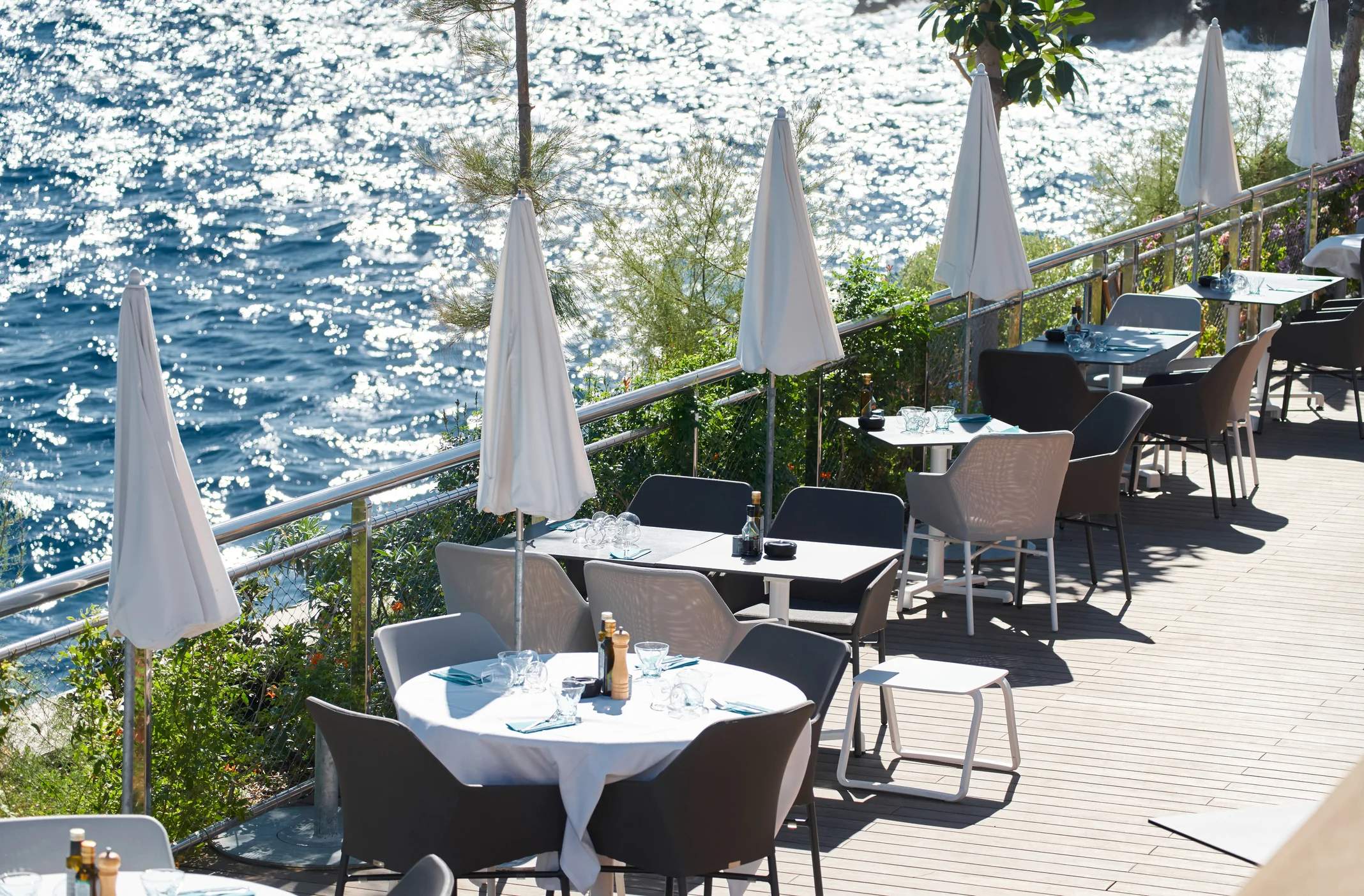 Outdoor restaurant patio with tables and umbrellas beside a sparkling blue sea.