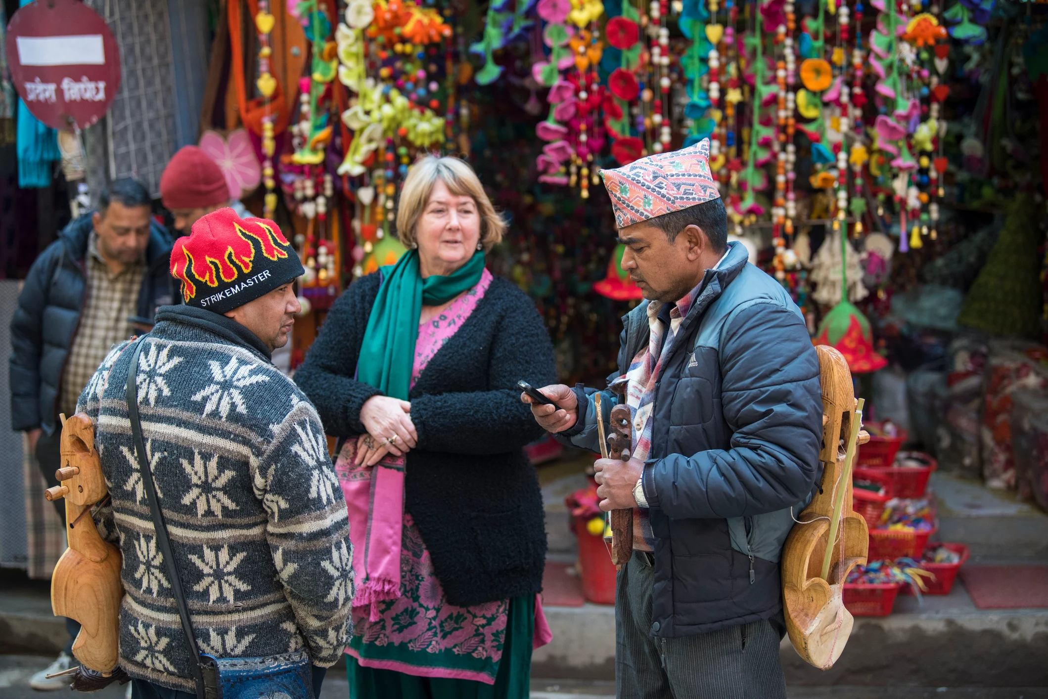 A woman chats with two men in a colorful market, surrounded by vibrant decorations and busy stalls.
