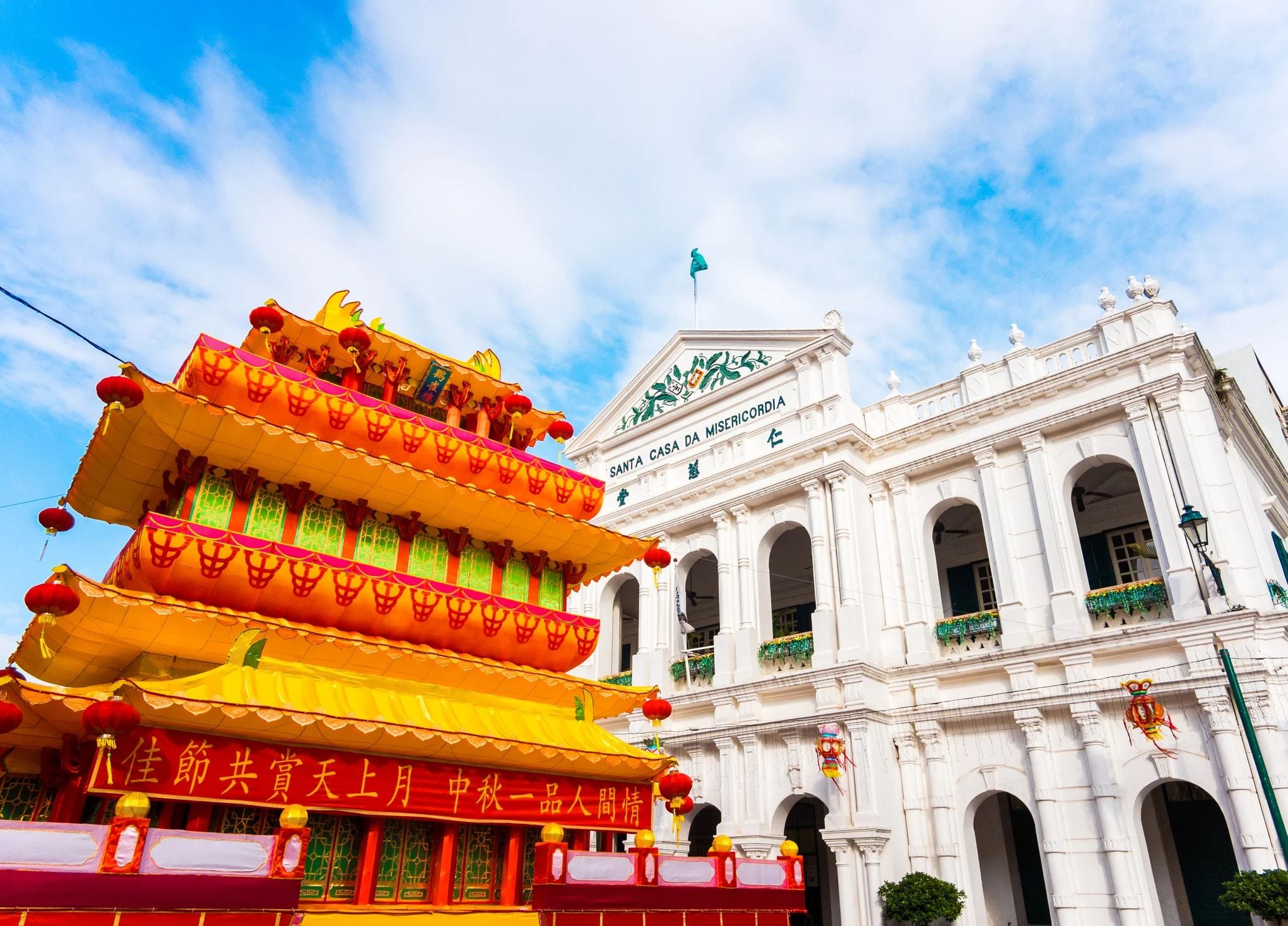 Colorful traditional decoration in front of a white colonial building, under a bright blue sky.