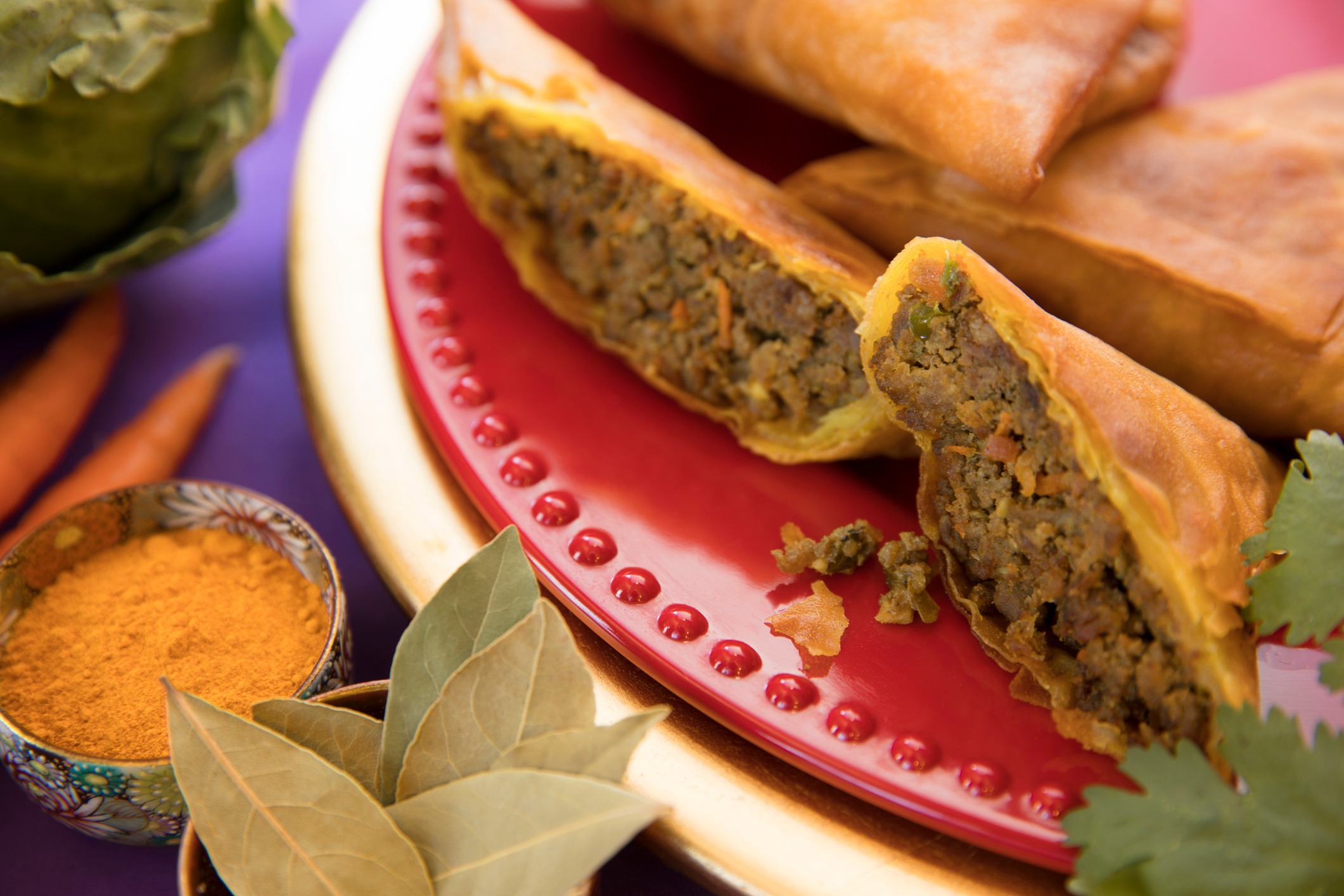 A plate of savory spring rolls filled with seasoned meat, surrounded by spices and fresh vegetables.