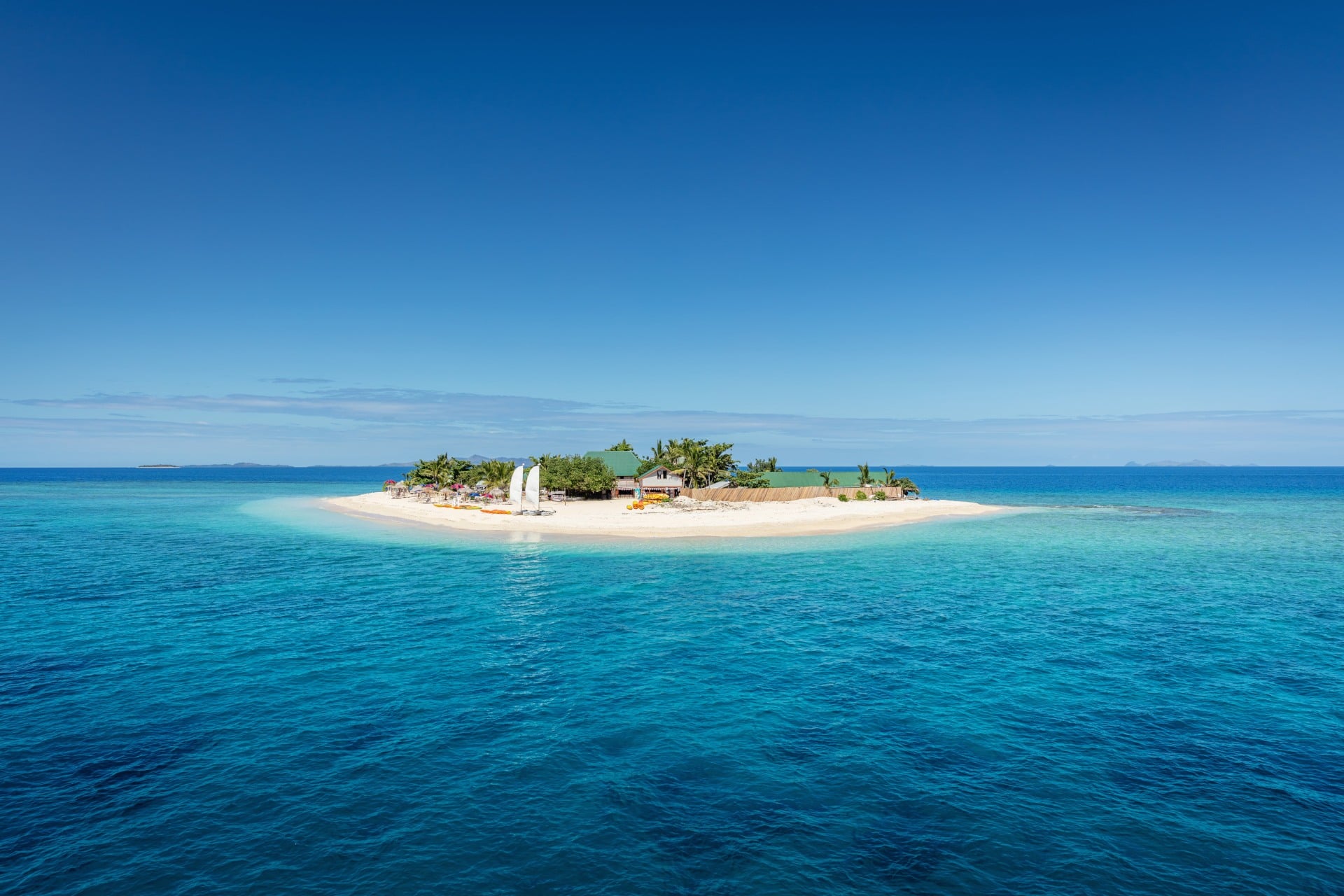 Beautiful small island in the middle of the south pacific ocean with beach huts, lounge chairs, palm trees, surrounded with beautiful clear turquoise water.