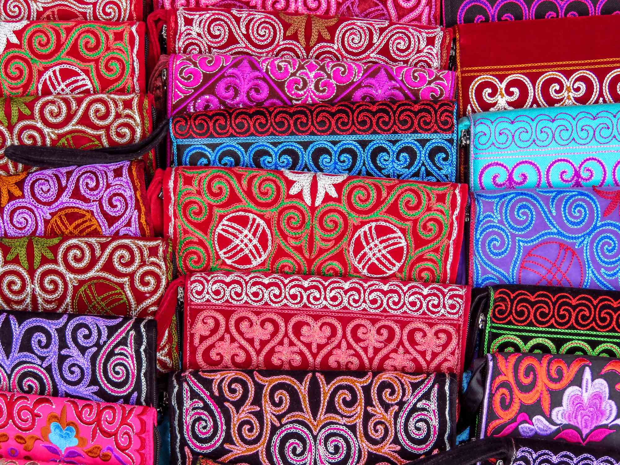 Colorful fabric pouches with intricate embroidery patterns in various shades of red, pink, blue, and black.