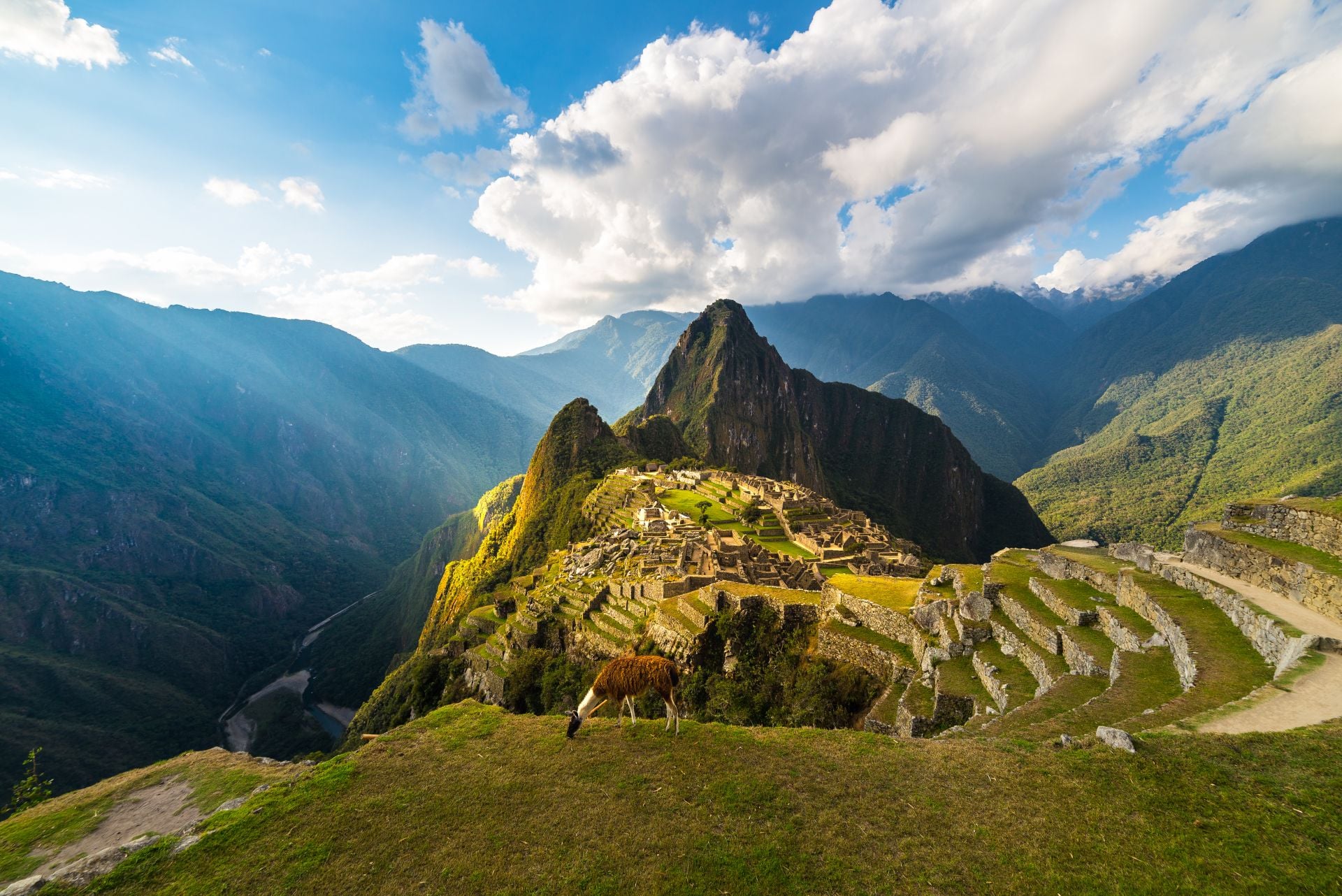 Machu Picchu illuminated by the warm sunset light. Wide angle view from the terraces above with scenic sky and sun burst