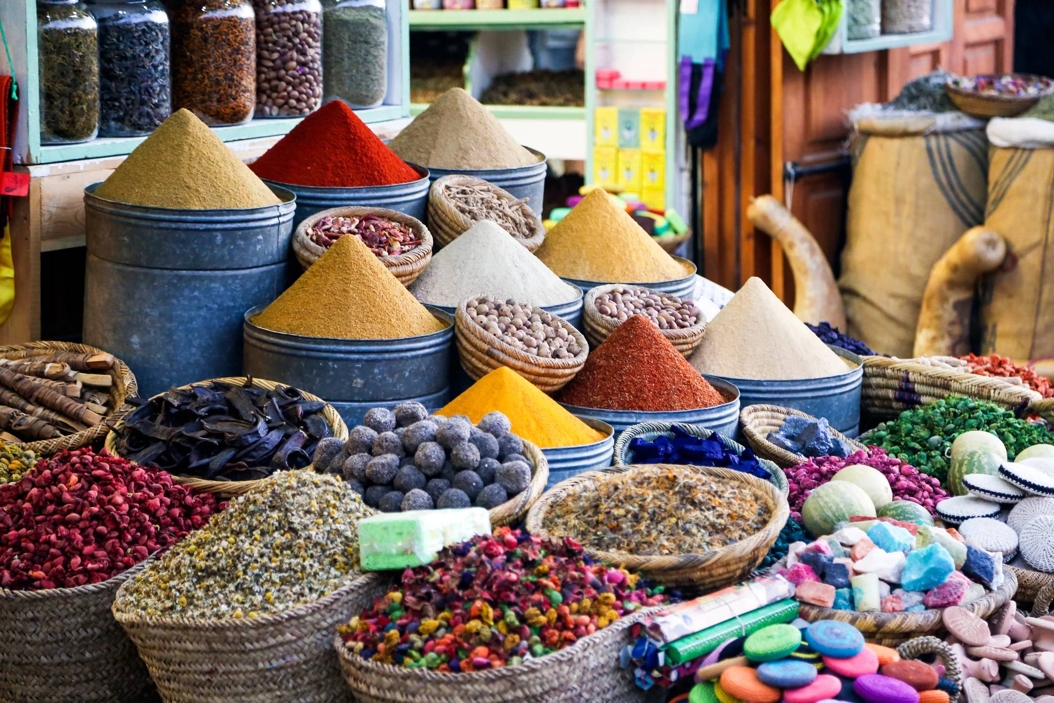 Colorful spices and herbs are displayed in baskets and metal containers at a vibrant market.